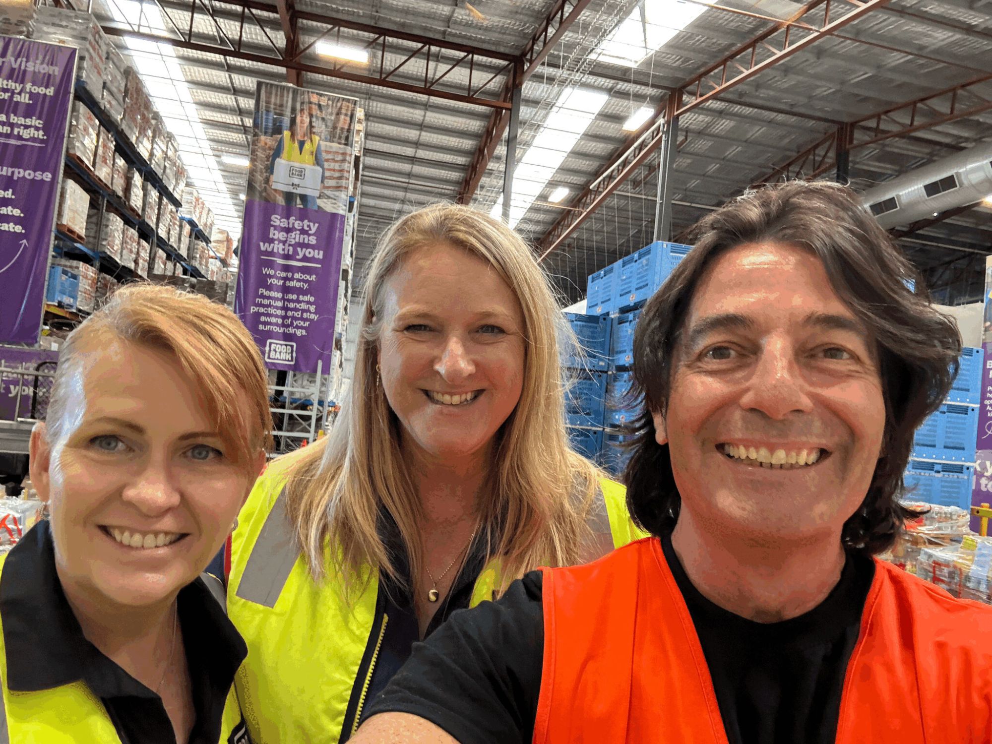 Three people in high-visibility vests inside Foodbank's Perth warehouse