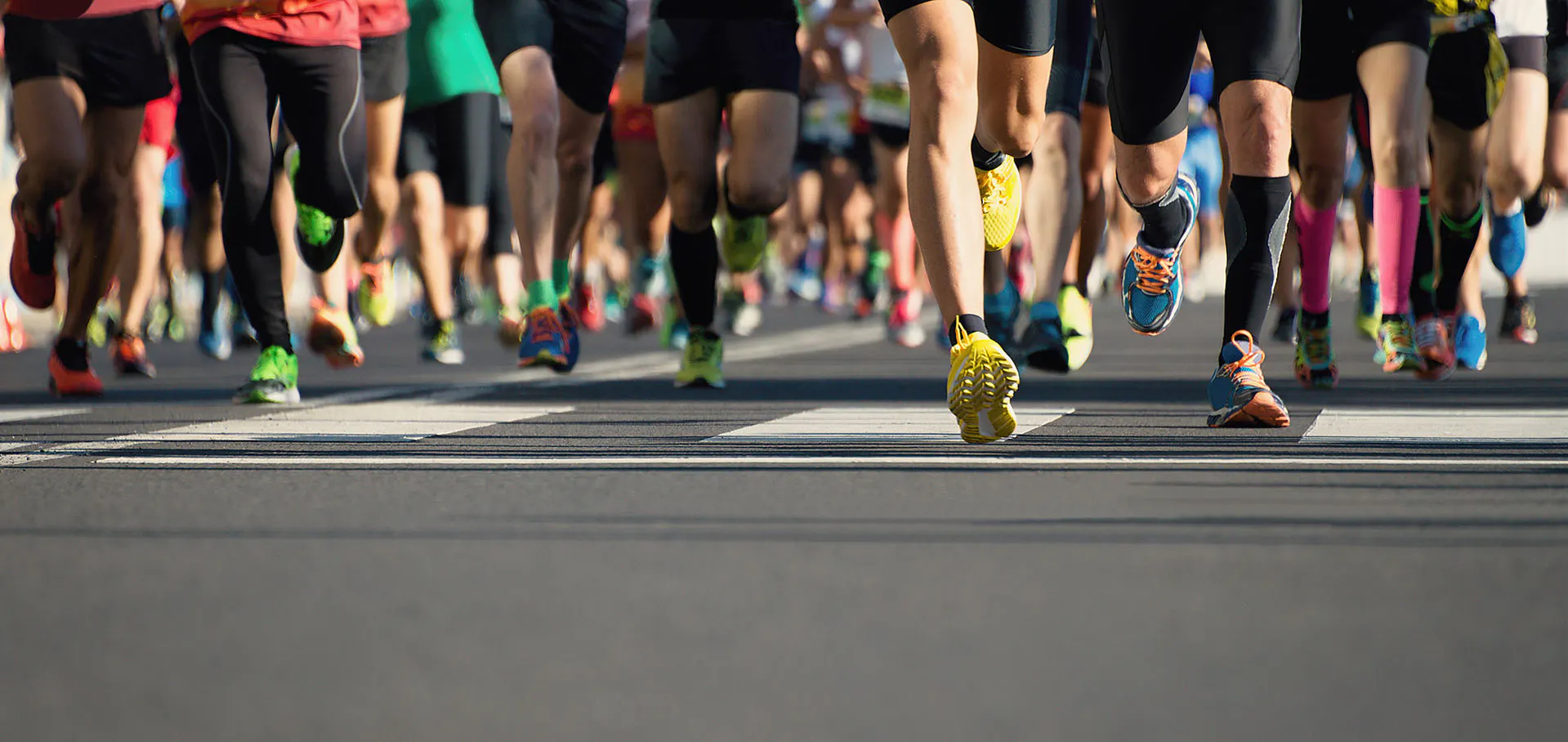 Image of a group of runners participating in a race. Colourful running shoes on the road