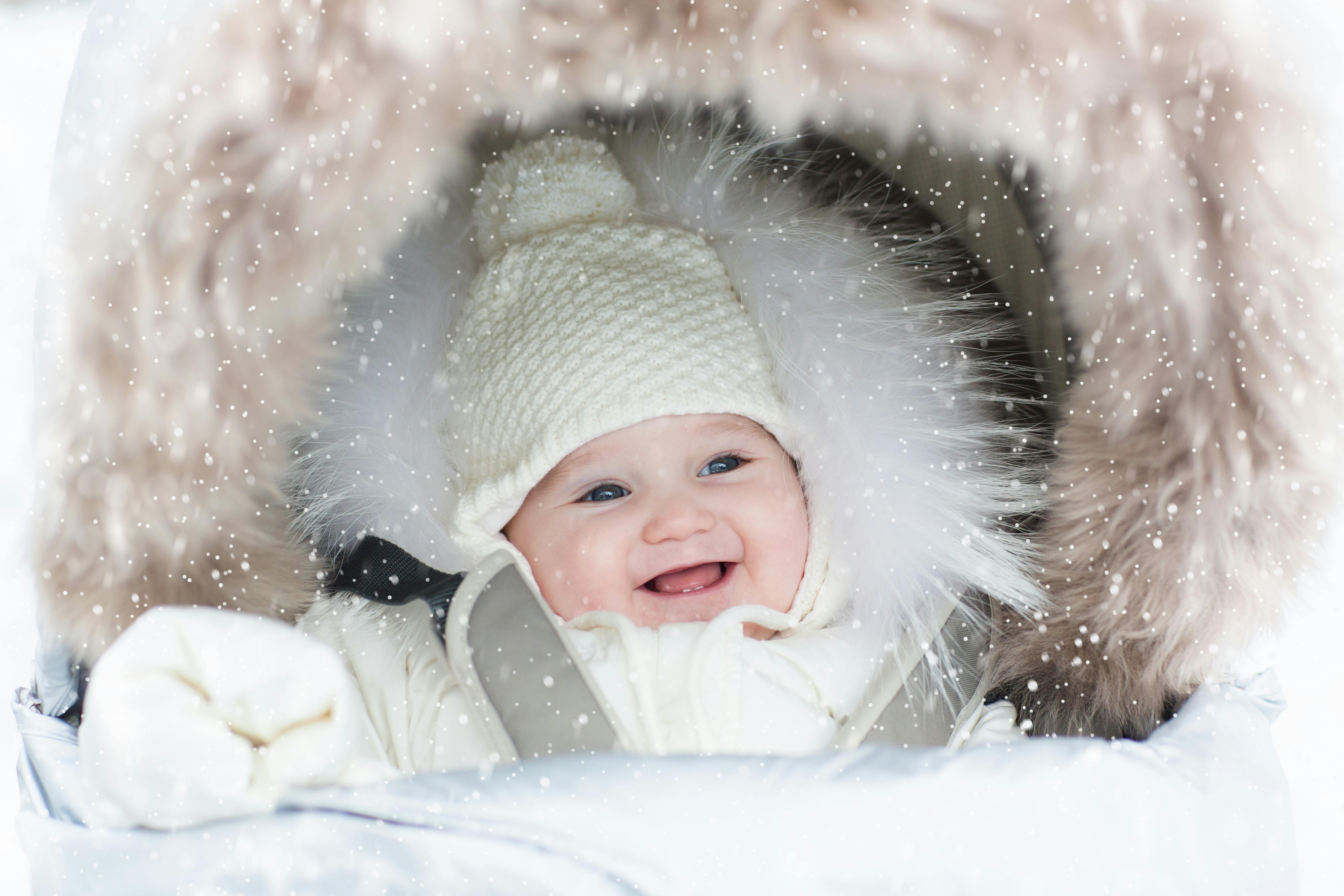 Glad bebis i vagn på vintern, snö som faller ned