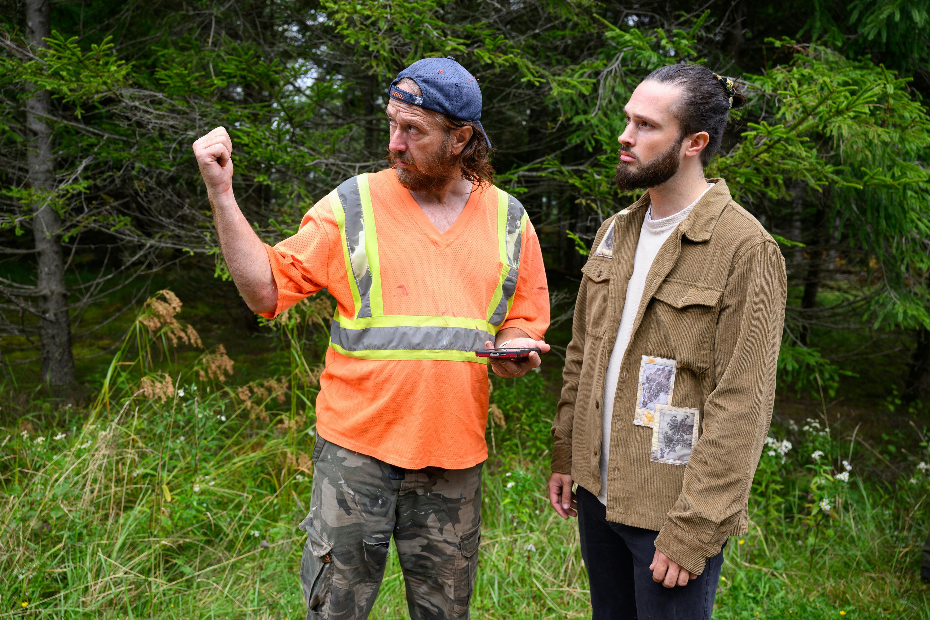 Person in neon orange shirt holding phone and giving directions to another person in a forest