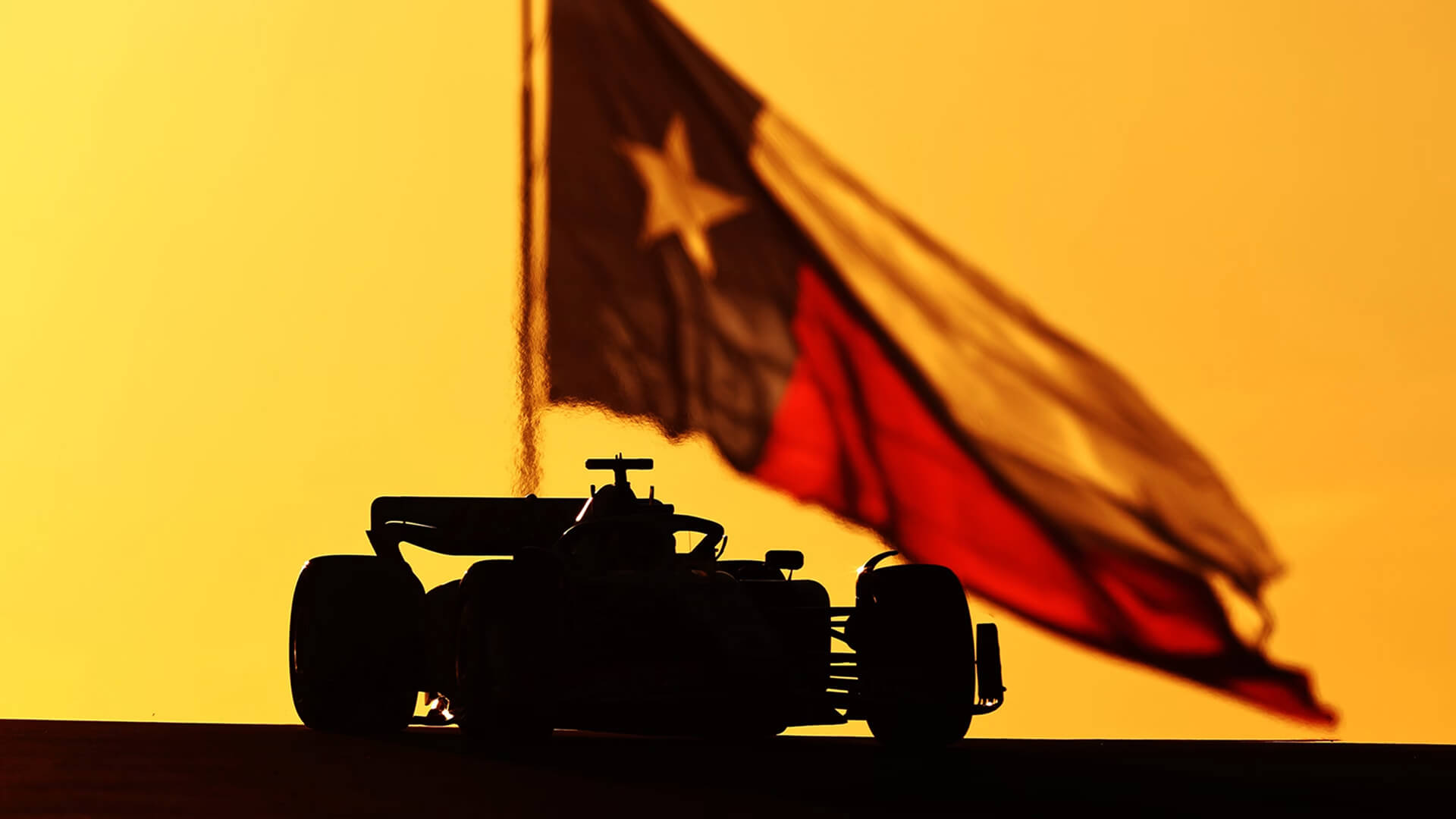 Silhouette of a Formula 1 car against a golden sky, with a Texas flag flying in the background.