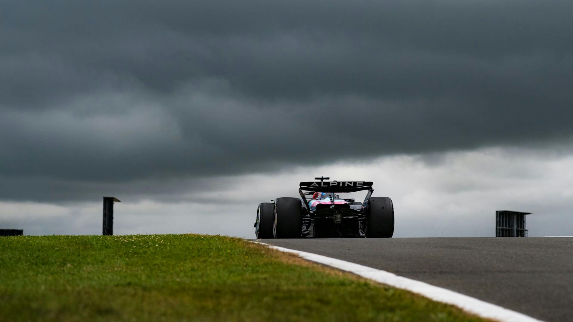 An F1 car speeding on the Silverstone track under dramatic, cloudy skies.