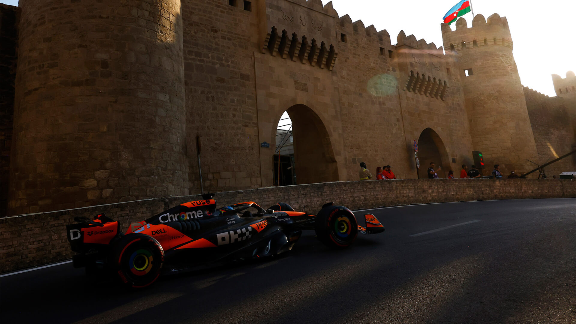 McLaren F1 car speeding past the historic Baku city walls under an Azerbaijan flag.