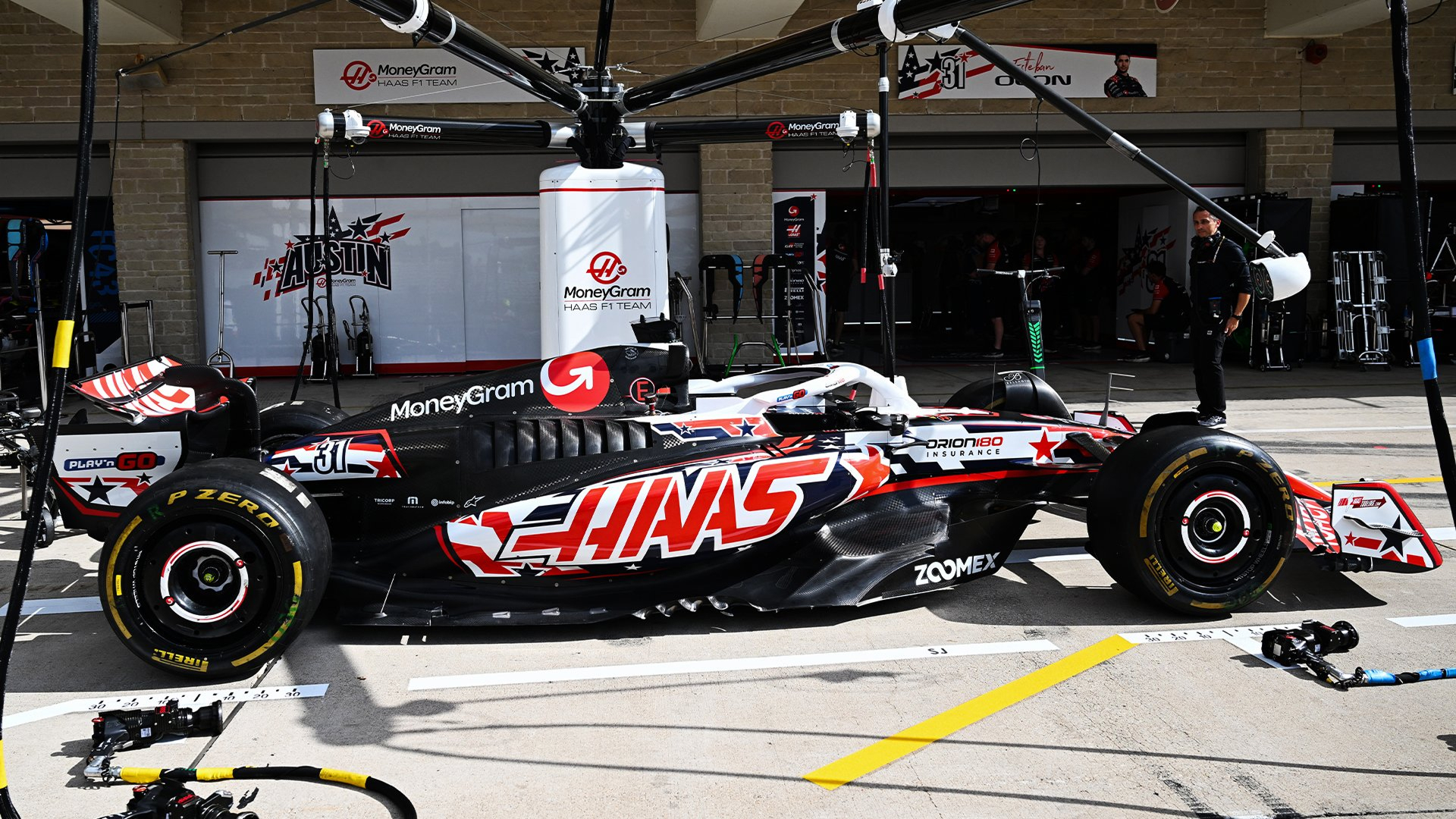 Haas F1 car in the garage at Circuit of the Americas (COTA), with mechanics and equipment visible around it.