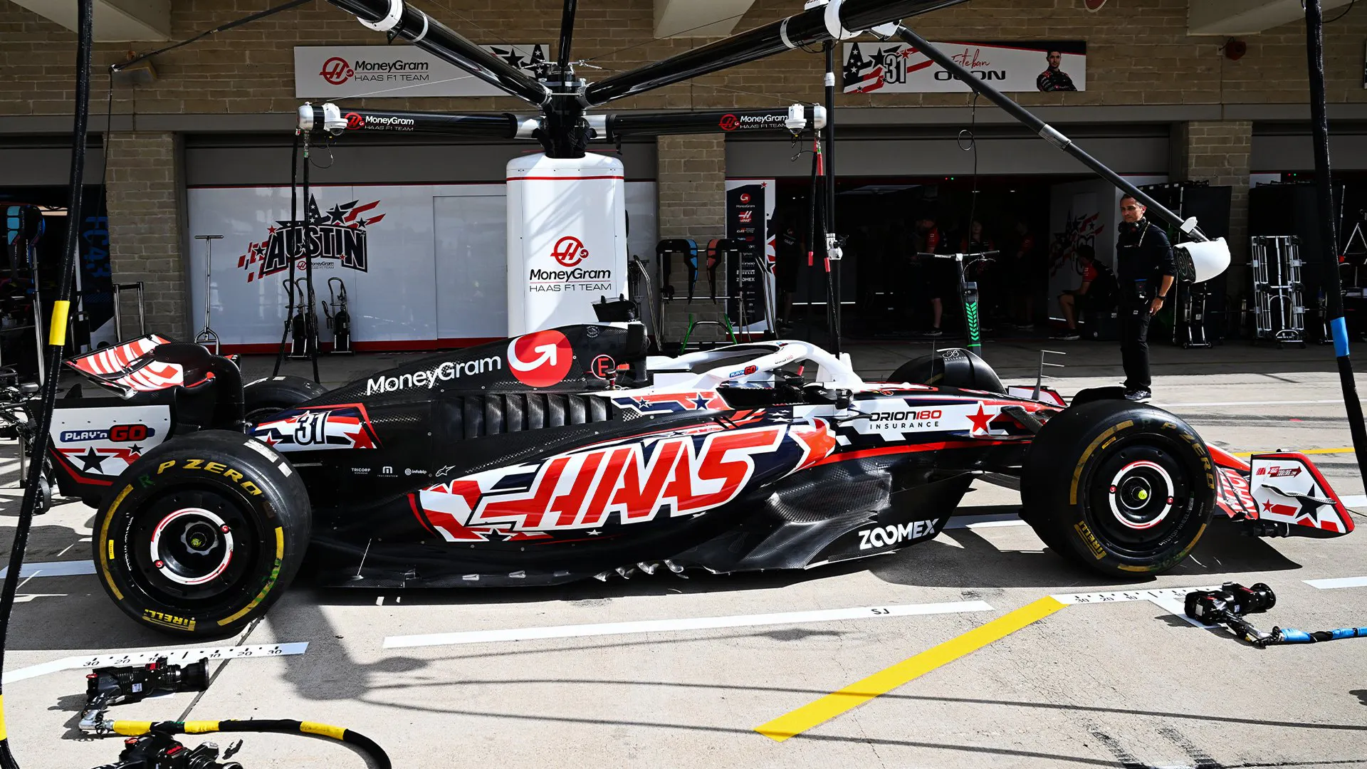 Haas F1 car in the garage at Circuit of the Americas (COTA), with mechanics and equipment visible around it.