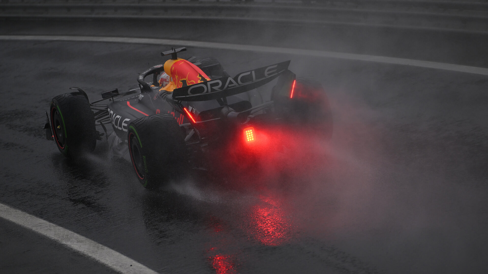 Verstappen in his Red Bull F1 car with rear rain lights on driving on a Interlagos wet track in 2024, spraying mist.
