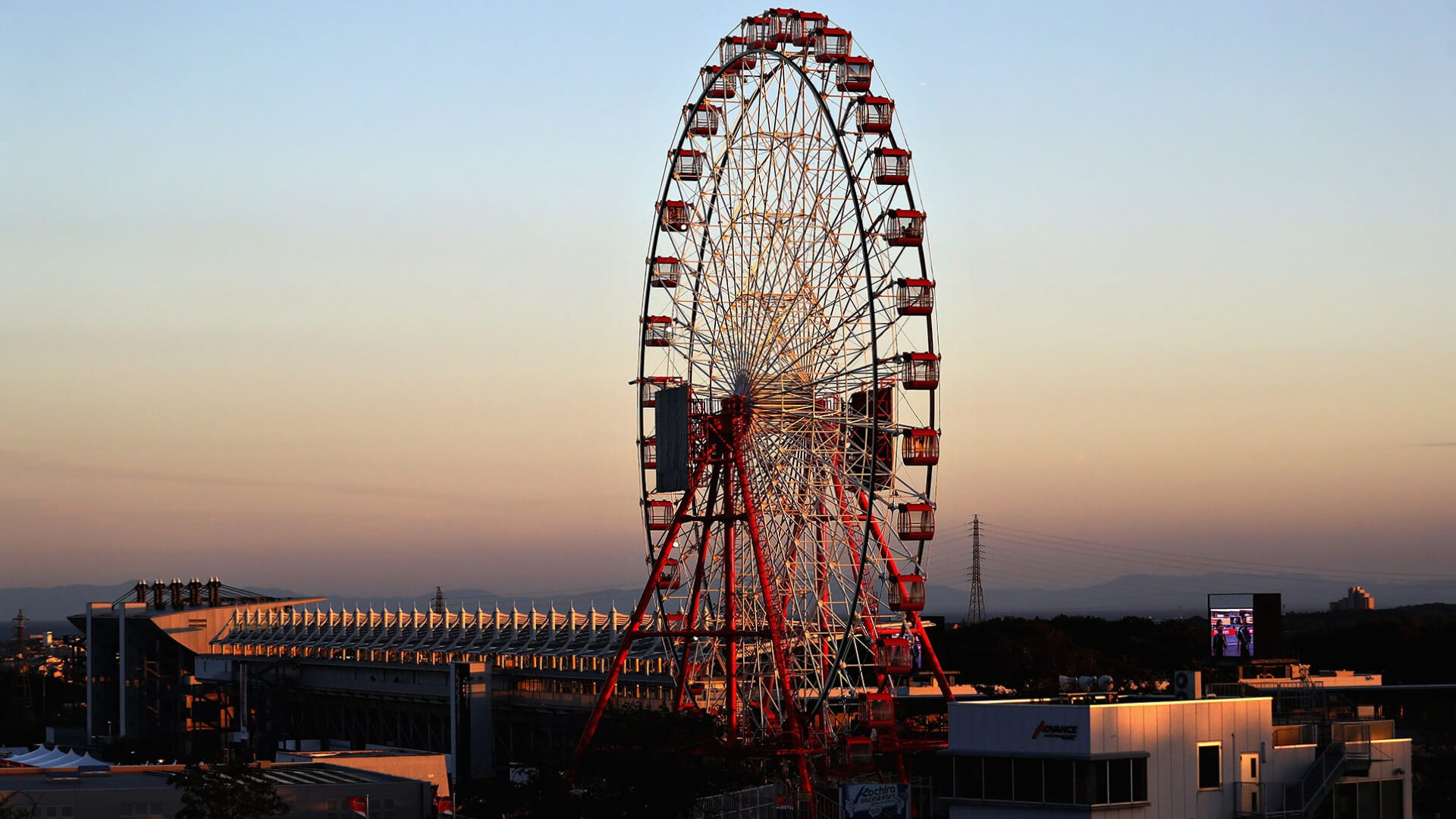 The iconic Suzuka Ferris wheel at sunset, overlooking the grandstands and track facilities of the Japanese Grand Prix circuit.