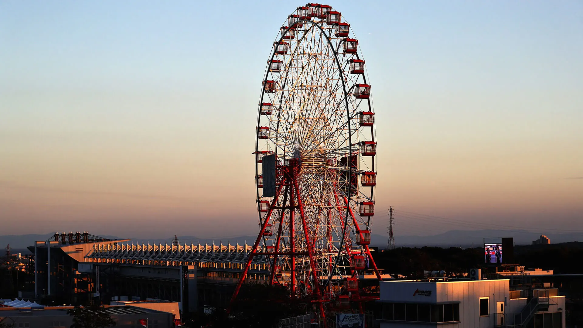 The iconic Suzuka Ferris wheel at sunset, overlooking the grandstands and track facilities of the Japanese Grand Prix circuit.