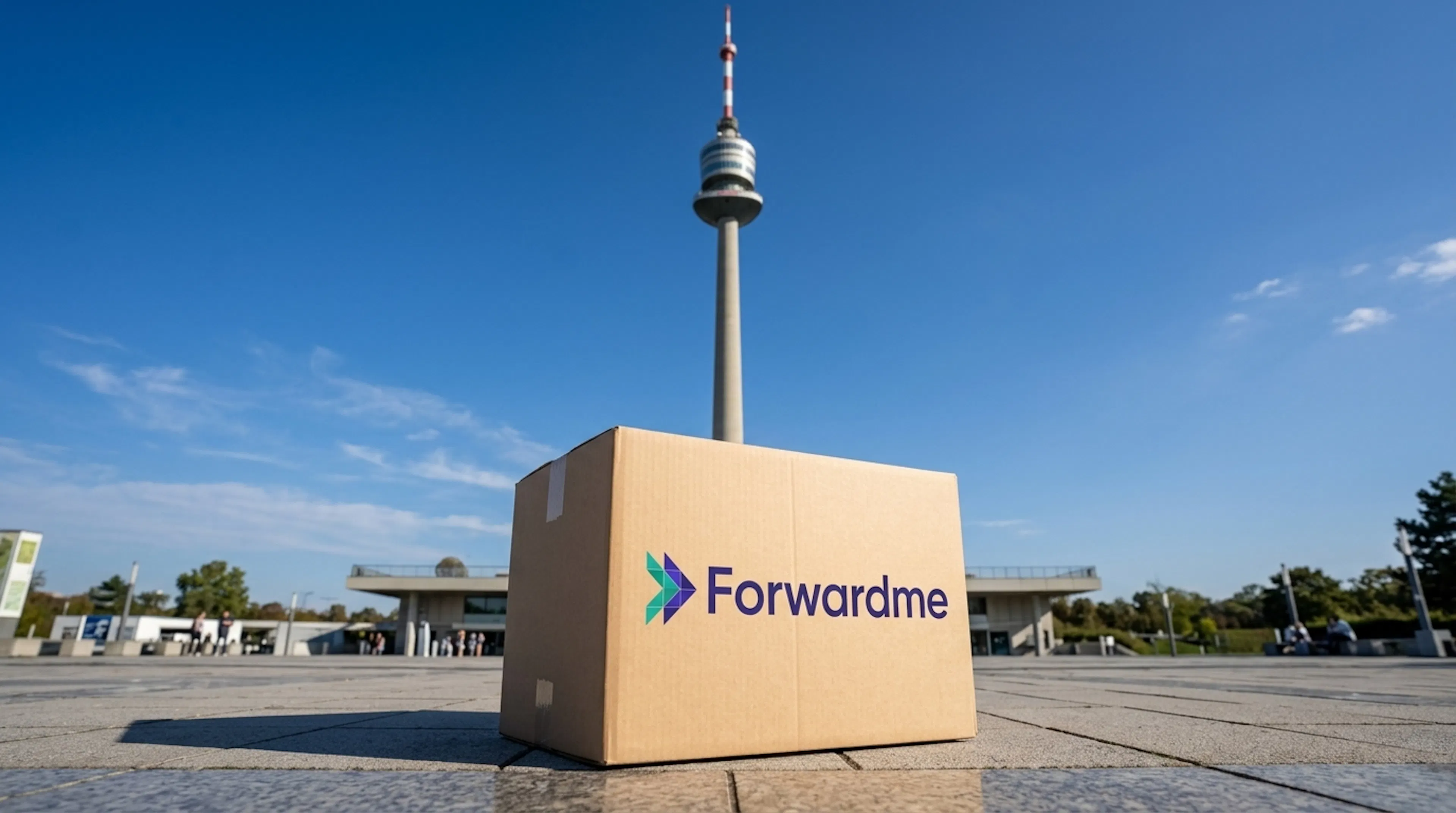 Cardboard box with “Forwardme” logo placed outdoors in Austria, with a Donauturm tower in the background under a clear blue sky.
