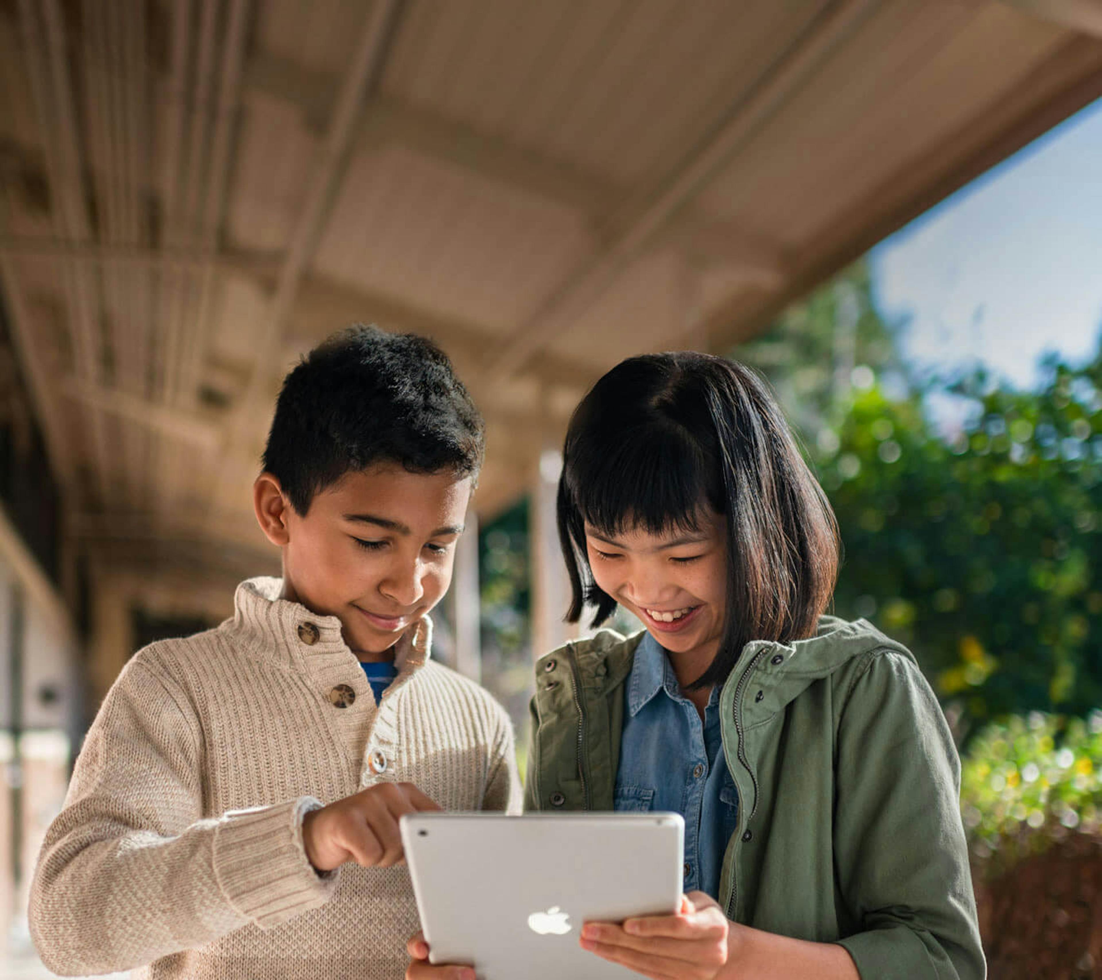 two young kids looking at their ipad outdoors