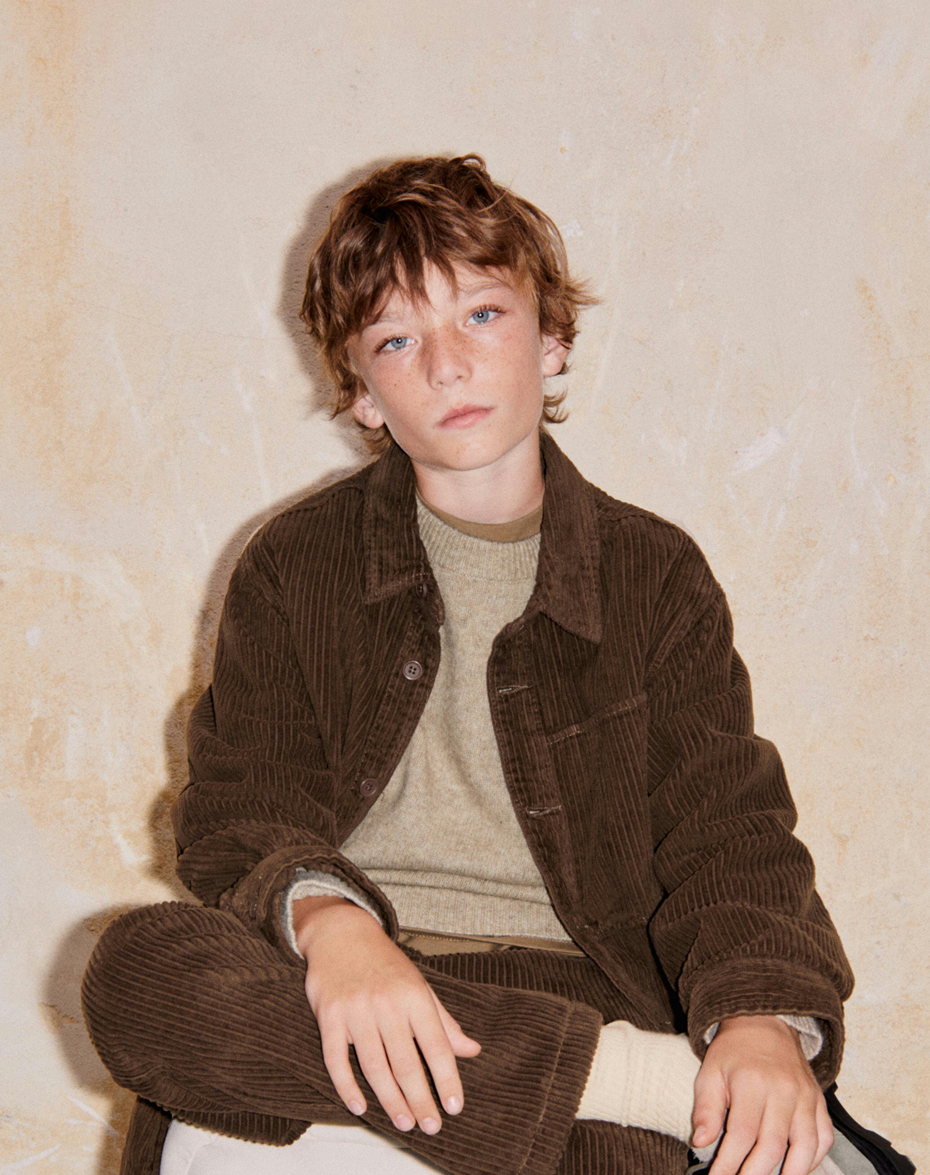 a young boy in a brown jacket sits on a cloud, in the style of eco-friendly craftsmanship
