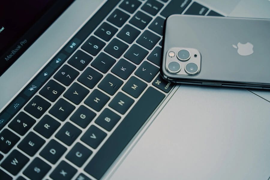 a silver iphone and an apple laptop by a keyboard