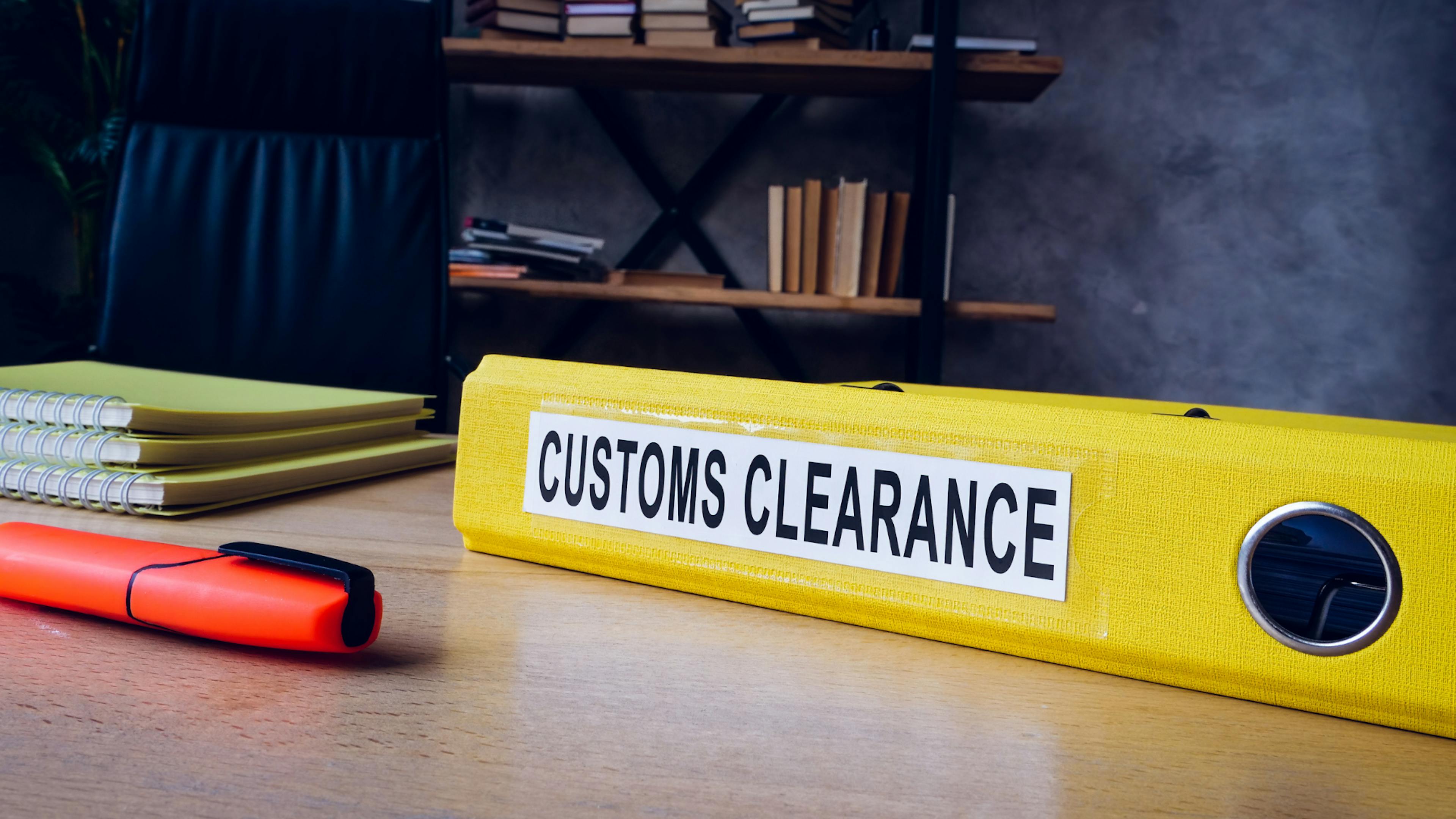 A file 'customs clearance' written on it on a desk with pen and other notebooks.