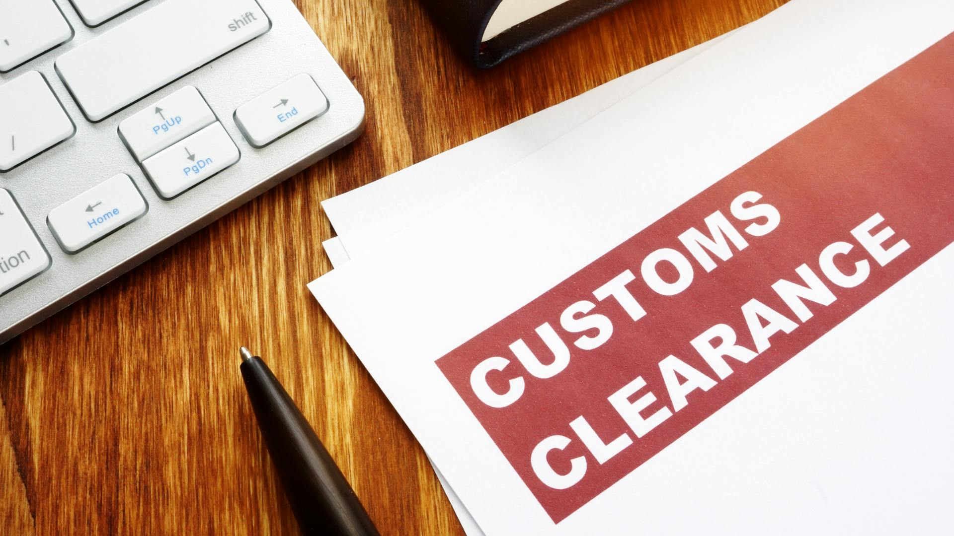 Papers written 'customs clearance' on them with a pen, laptop on a work desk.