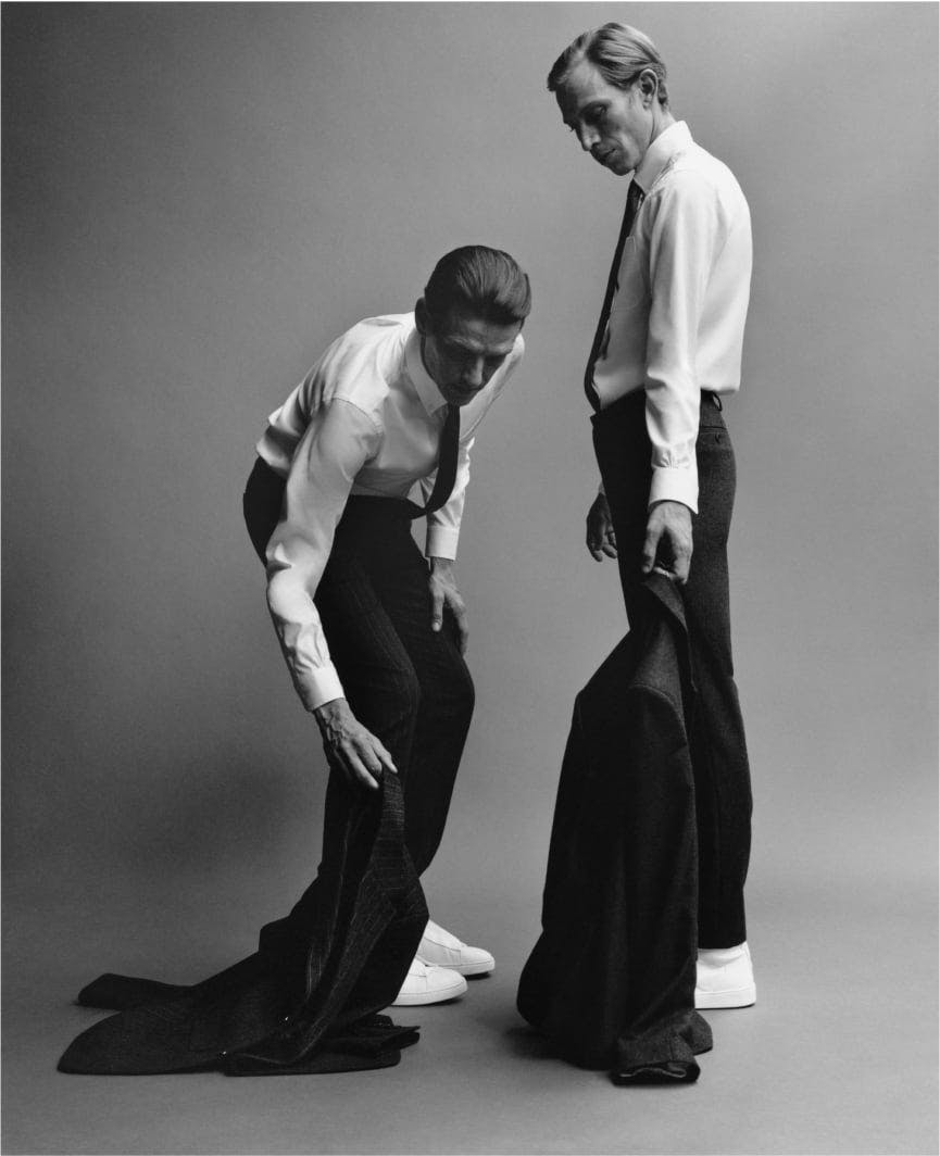 two men bending down ready to tie their coat pants, in the style of stark black-and-white photography