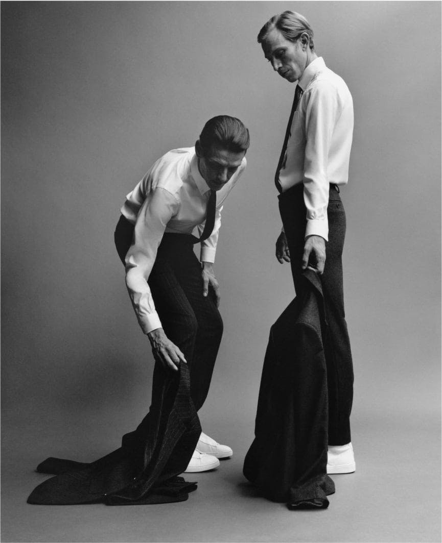 two men bending down ready to tie their coat pants, in the style of stark black-and-white photography two men bending down ready to tie their coat pants, in the style of stark black-and-white photography
