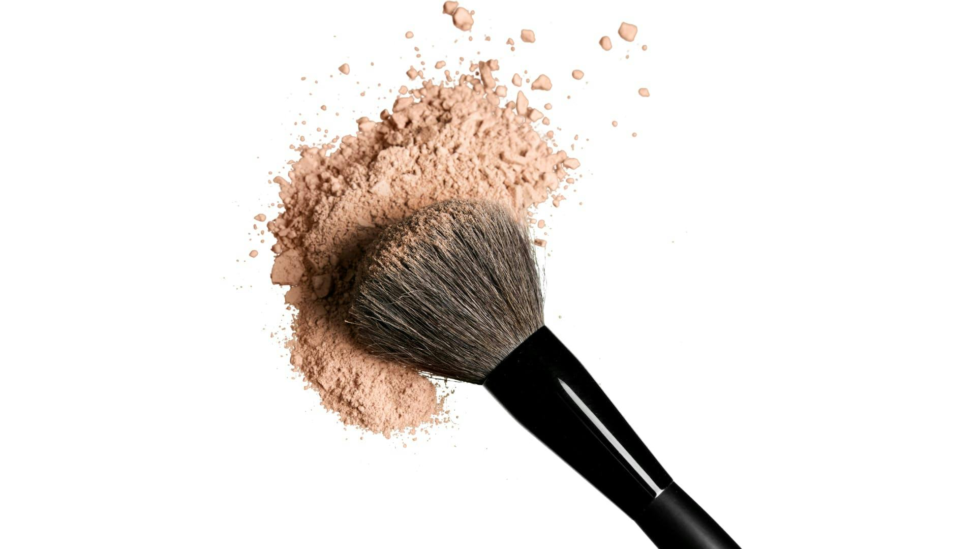 A make-up brush with make-up scattering around. A make-up brush with make-up scattering around.