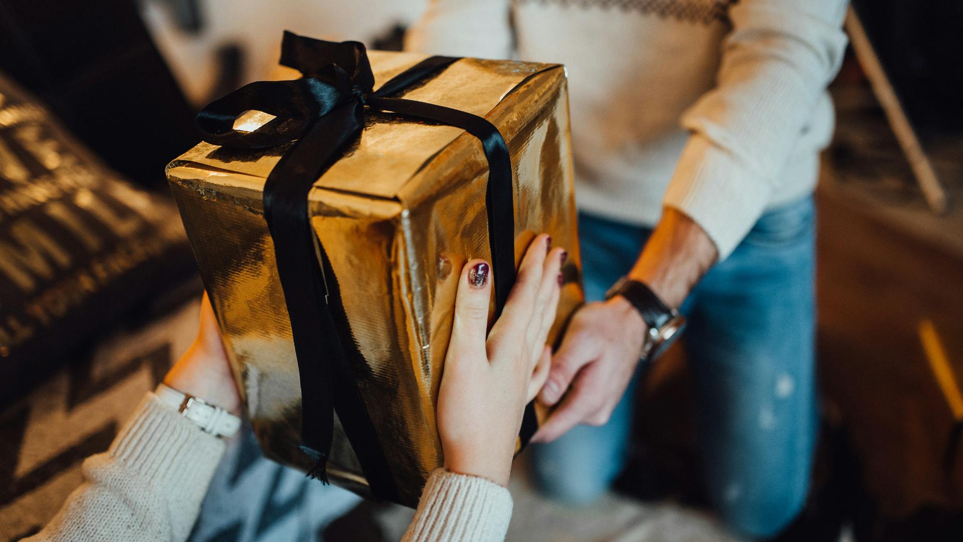 Woman giving a man big gift package to a man who is wearing a watch. 