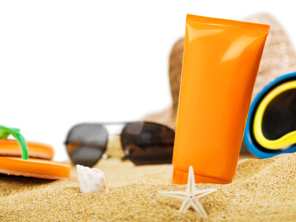 Beach gearsi like sunglasses, sandals, and sunscreen creams on the sand. 