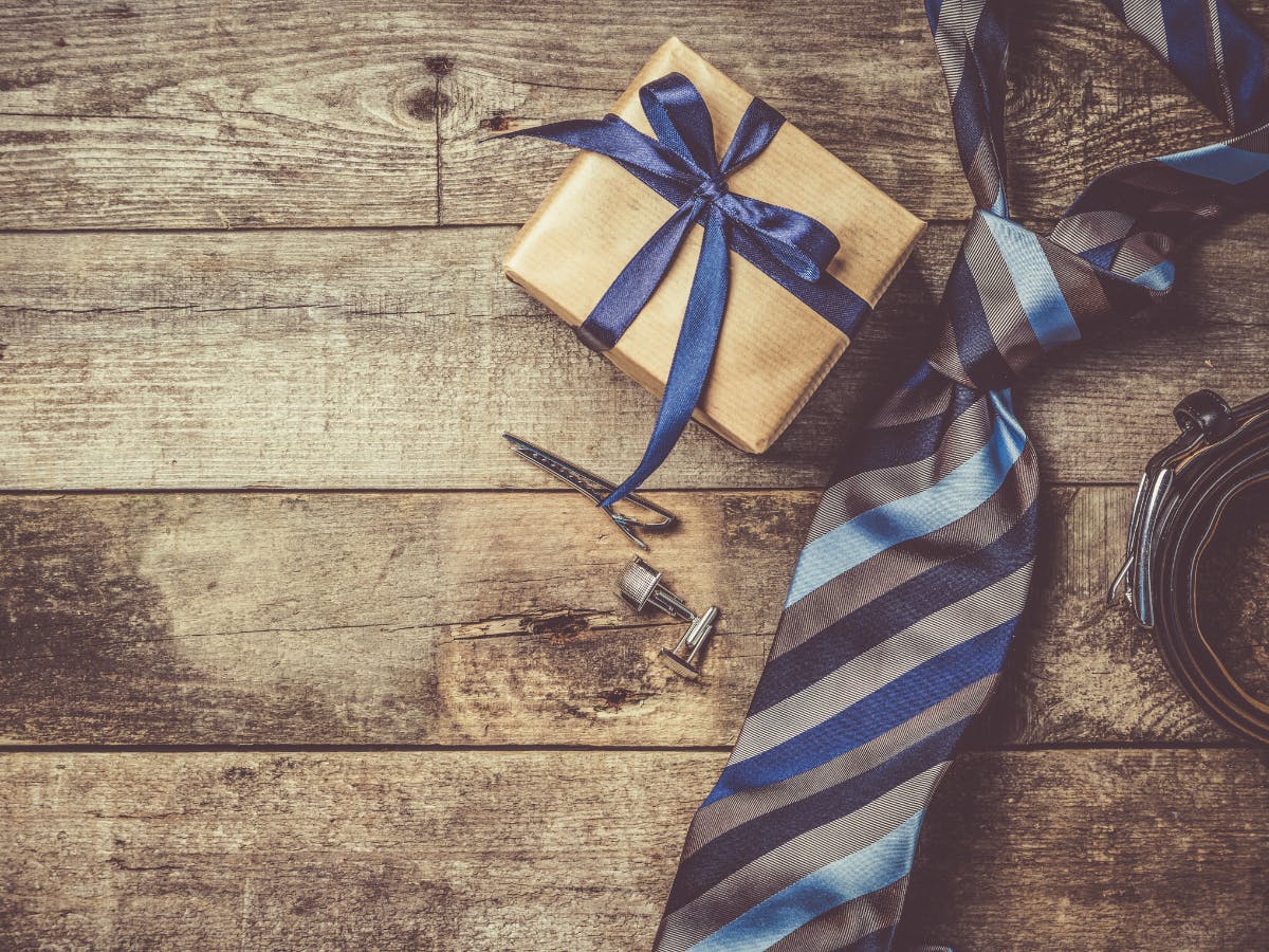 On a wooden desk there is a tie, belt and a gift package. 