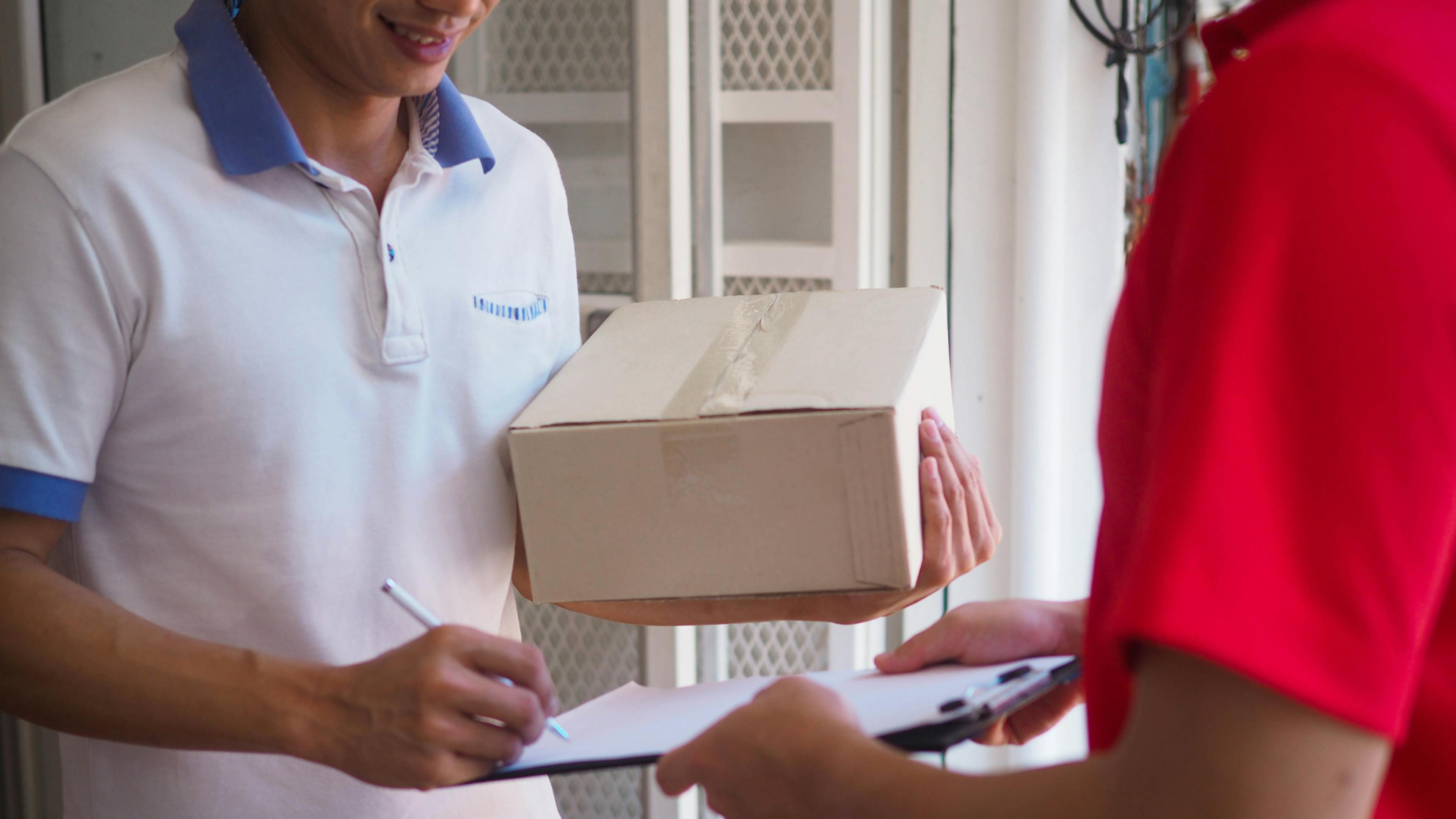 A delivery man delivering a package to customer, customer signing papers to receive the package. 