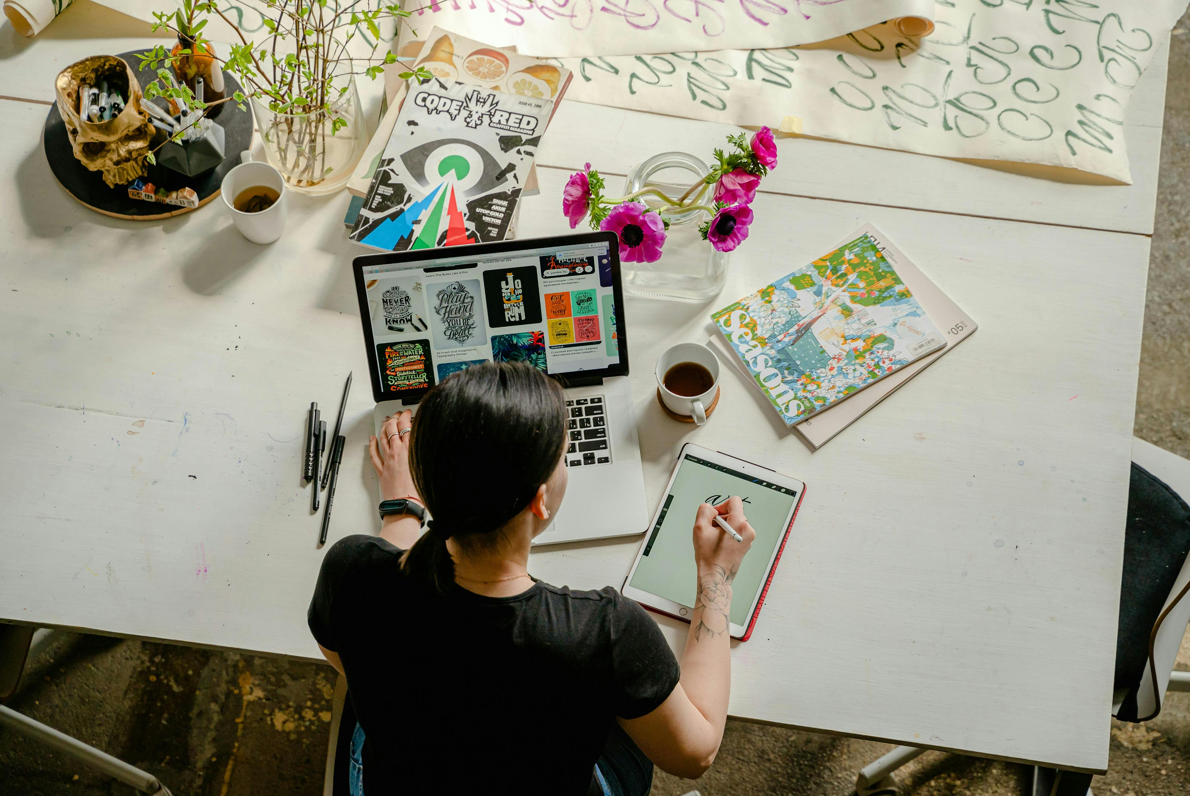 A woman working on a tablet while looking at the laptop as well. 