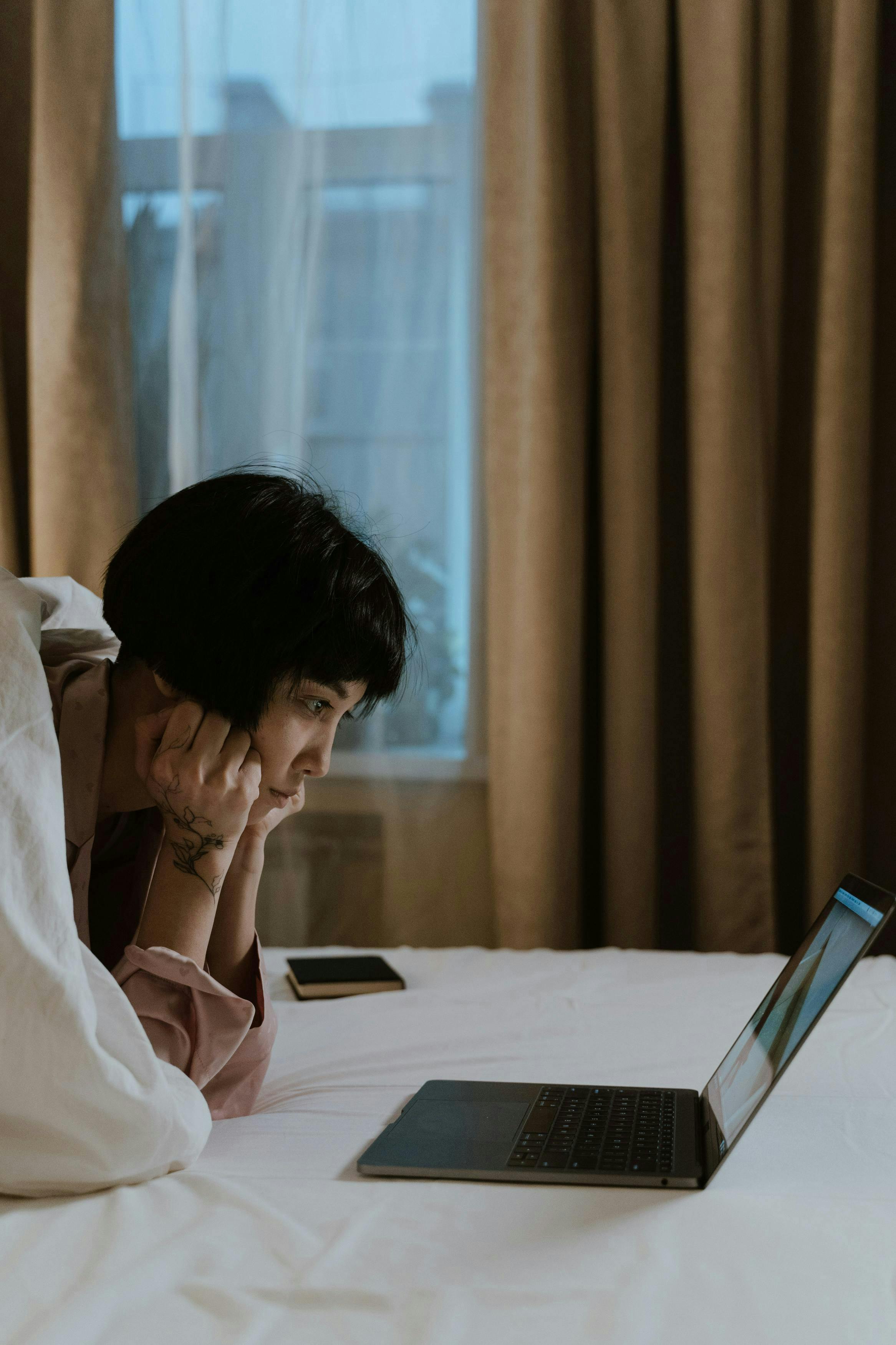 A woman looking at the laptop from her bed. 