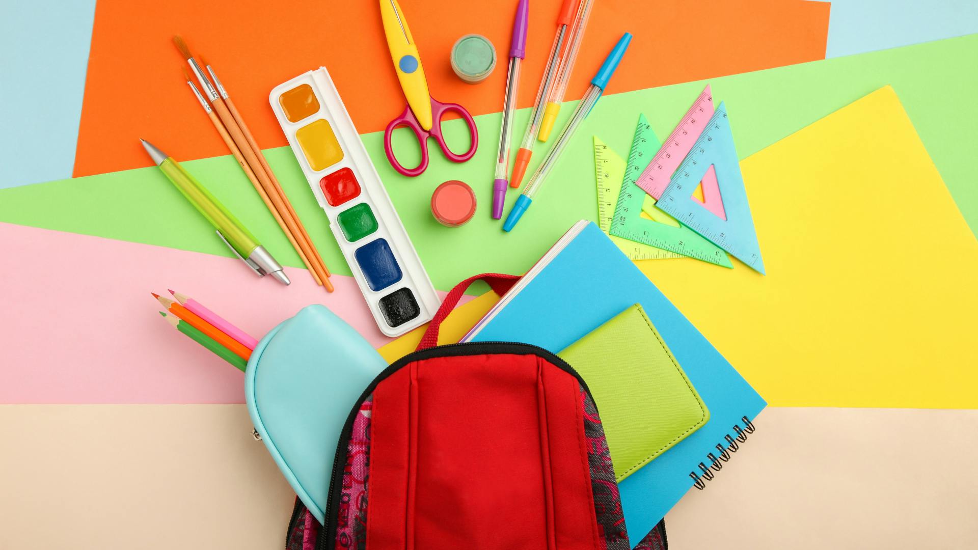 Different type of school supplies on a colorful background.