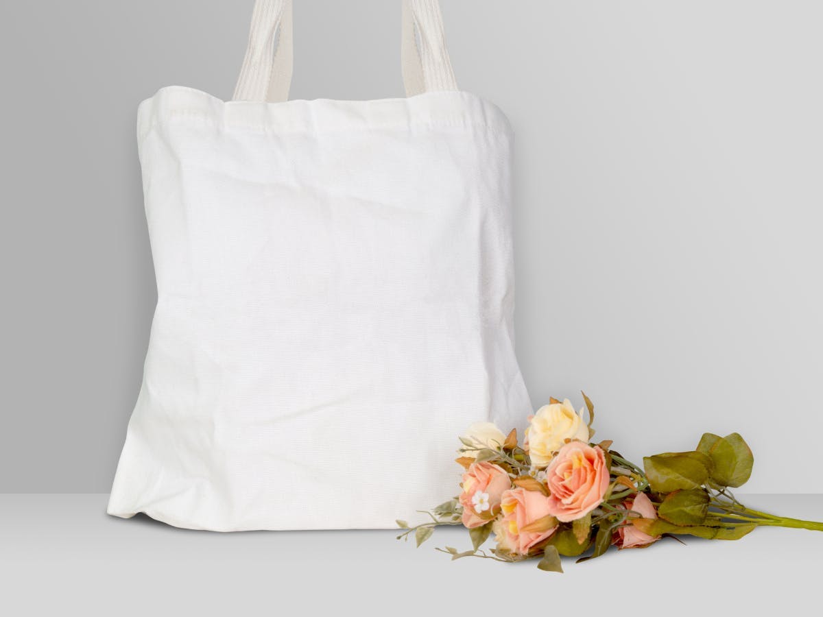 A white tote bag, and a pink flower in front of it. 