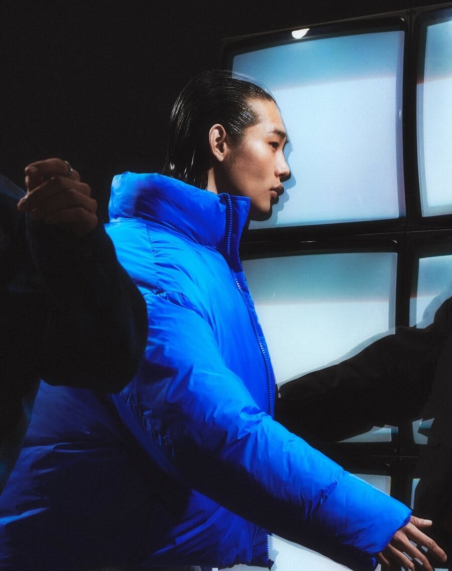 three men facing the big screens, in their blue puffer coats