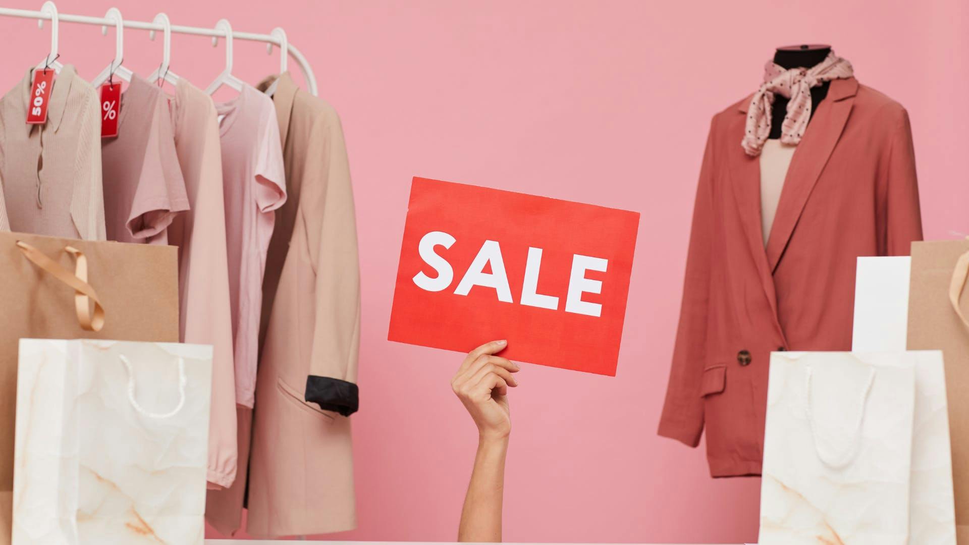 A clothing rack on the left with 2 packages in front of it, a manequin on the right with 2 packages too, and one hand rised holding a paper states Sale. 