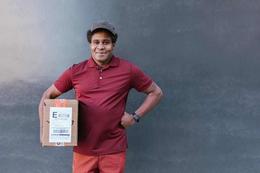 a delivery male holds a box in front of a wall