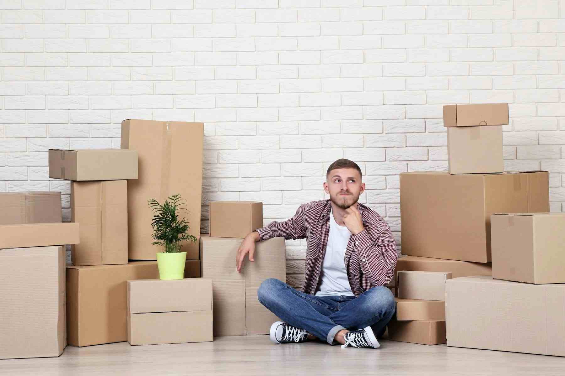 A man sitting on the floor next to a box of shipping boxes.