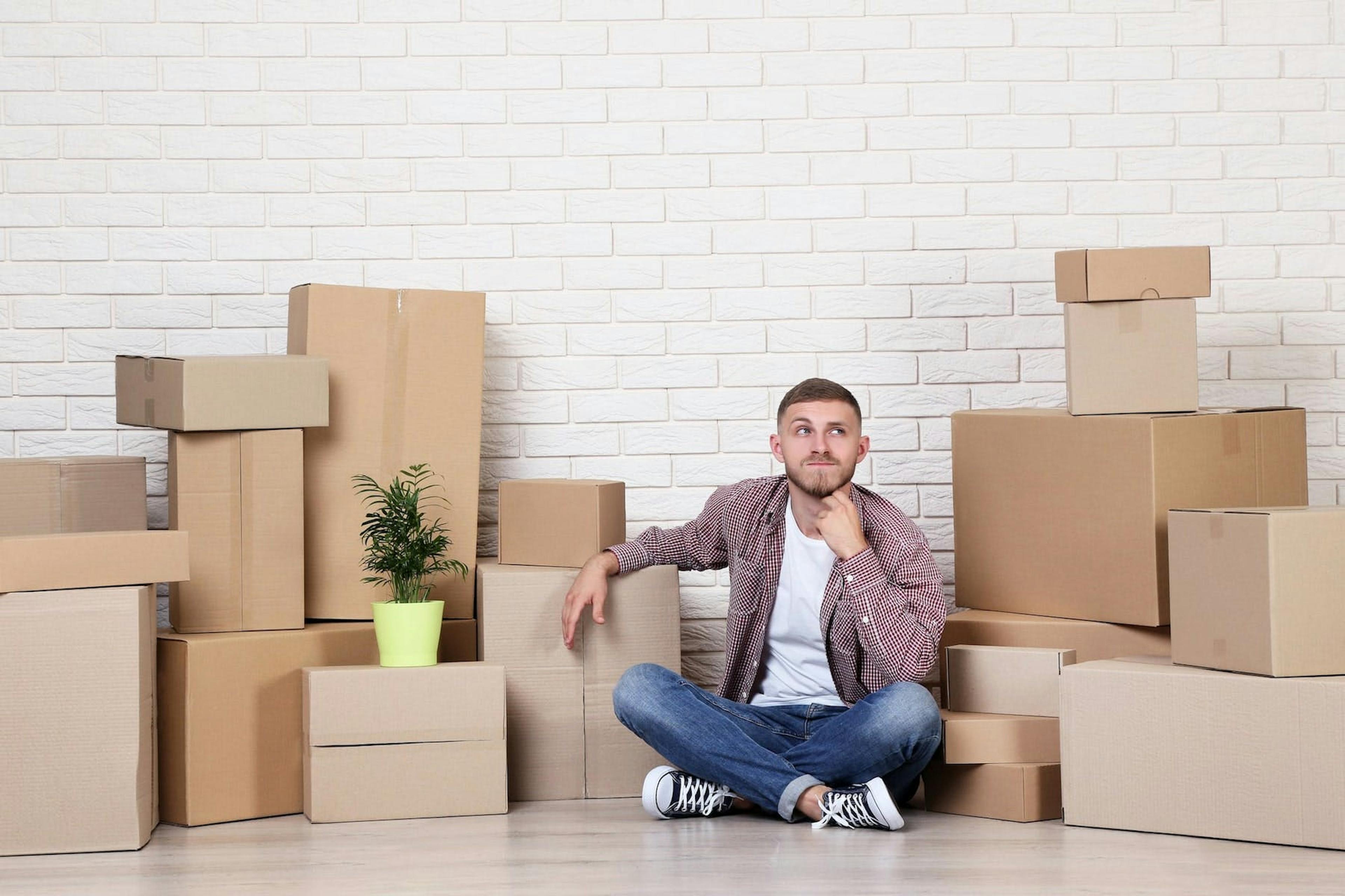 a man sitting on the floor next to a box of shipping boxes, in the style of non-functional design, soft, dream-like quality
