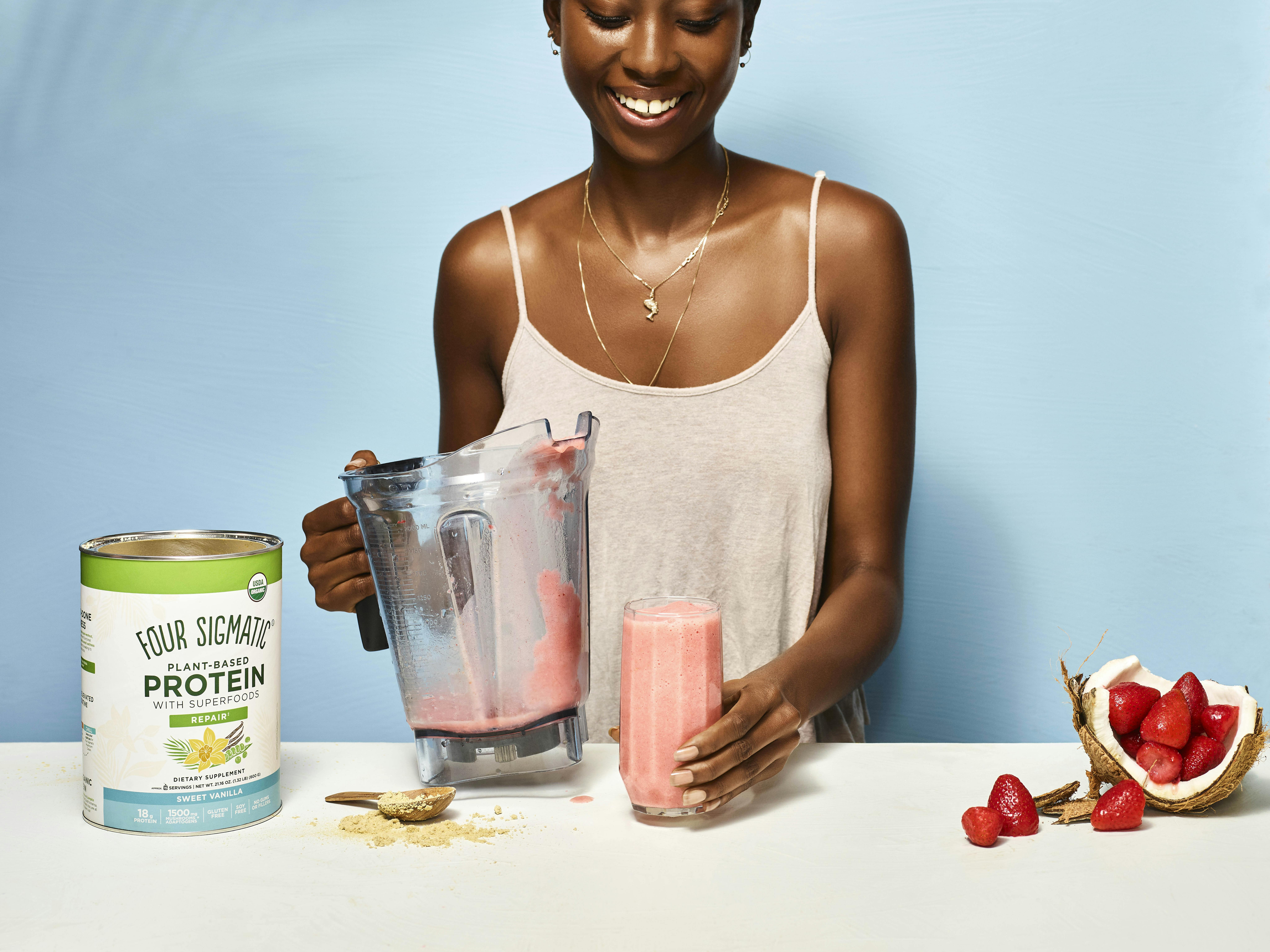 Woman making a strawberry smoothie using Four Sigmatic Plant-based Protein Sweet Vanilla