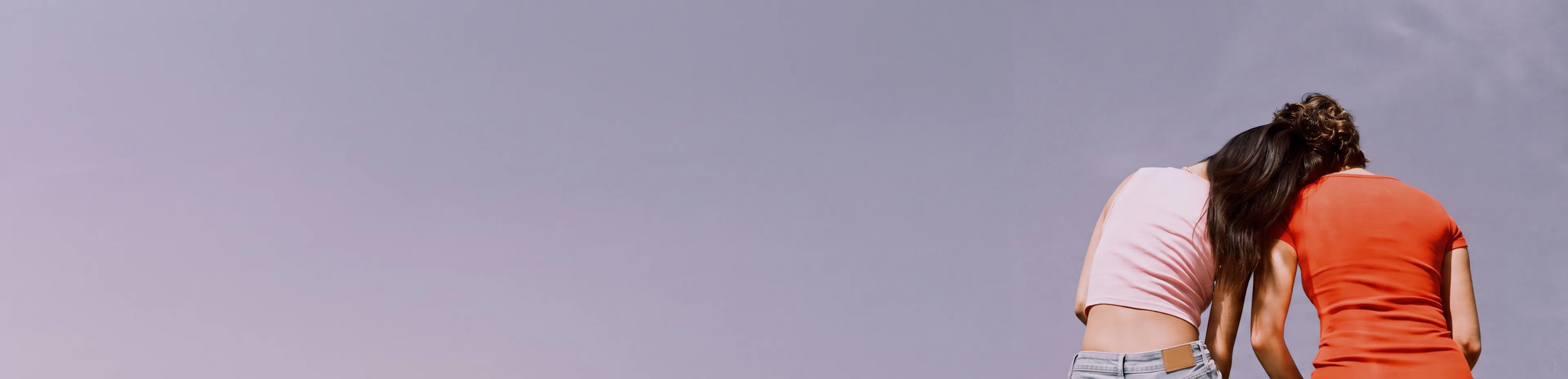 Two young people leaning together against open sky