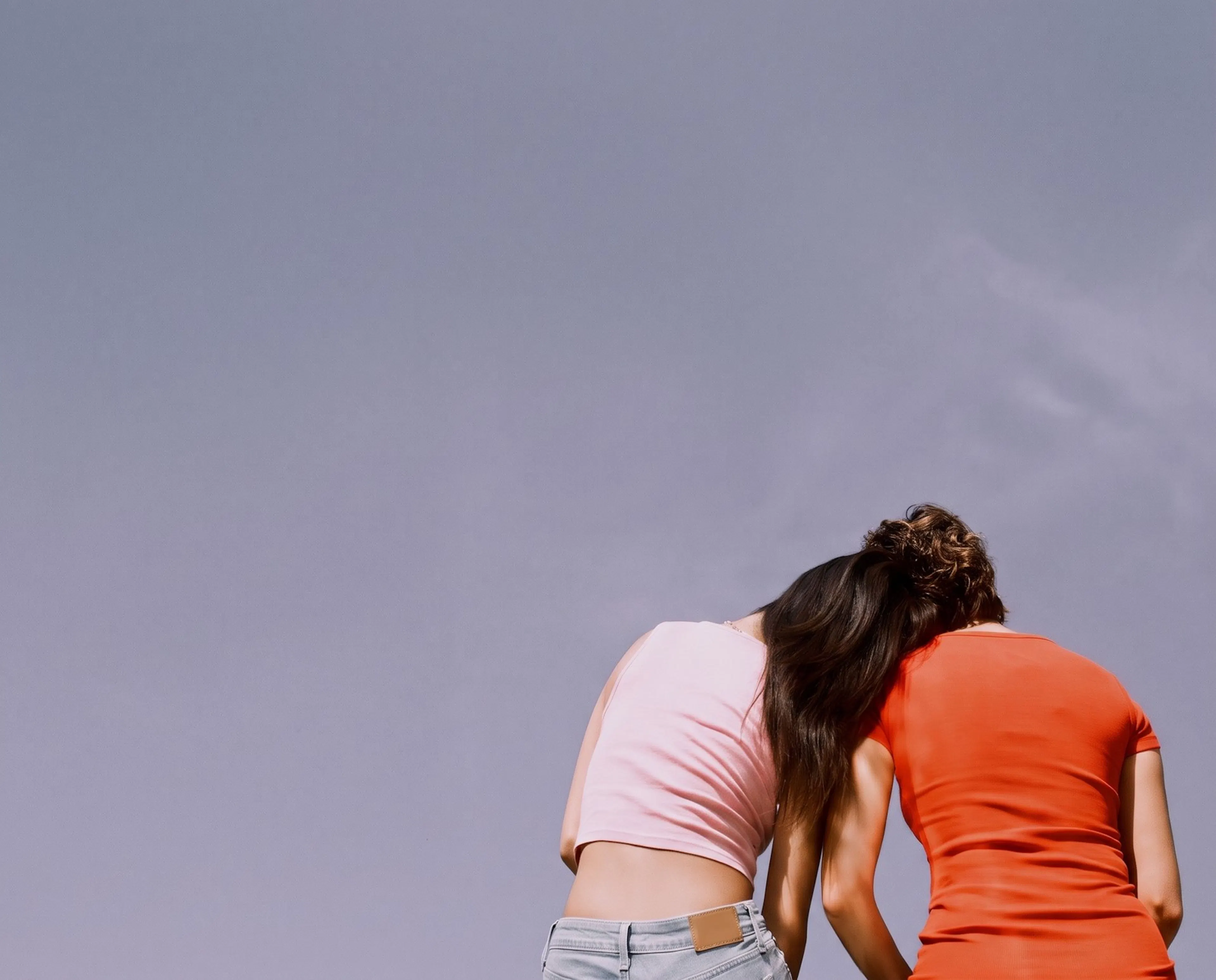 Two young people leaning together against open sky