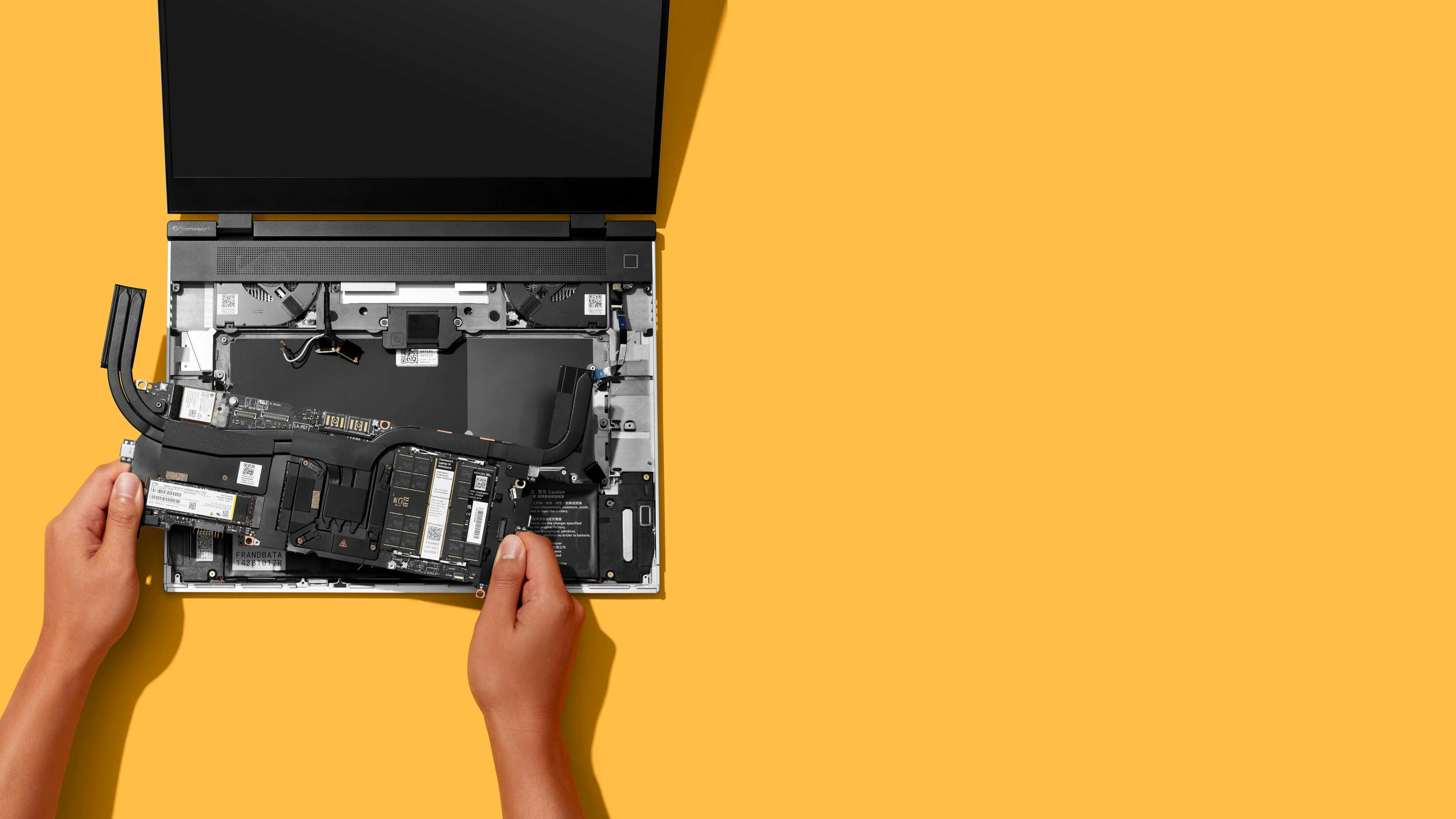 Top-down studio shot of a Framework Laptop 16 with a person installing the mainboard.