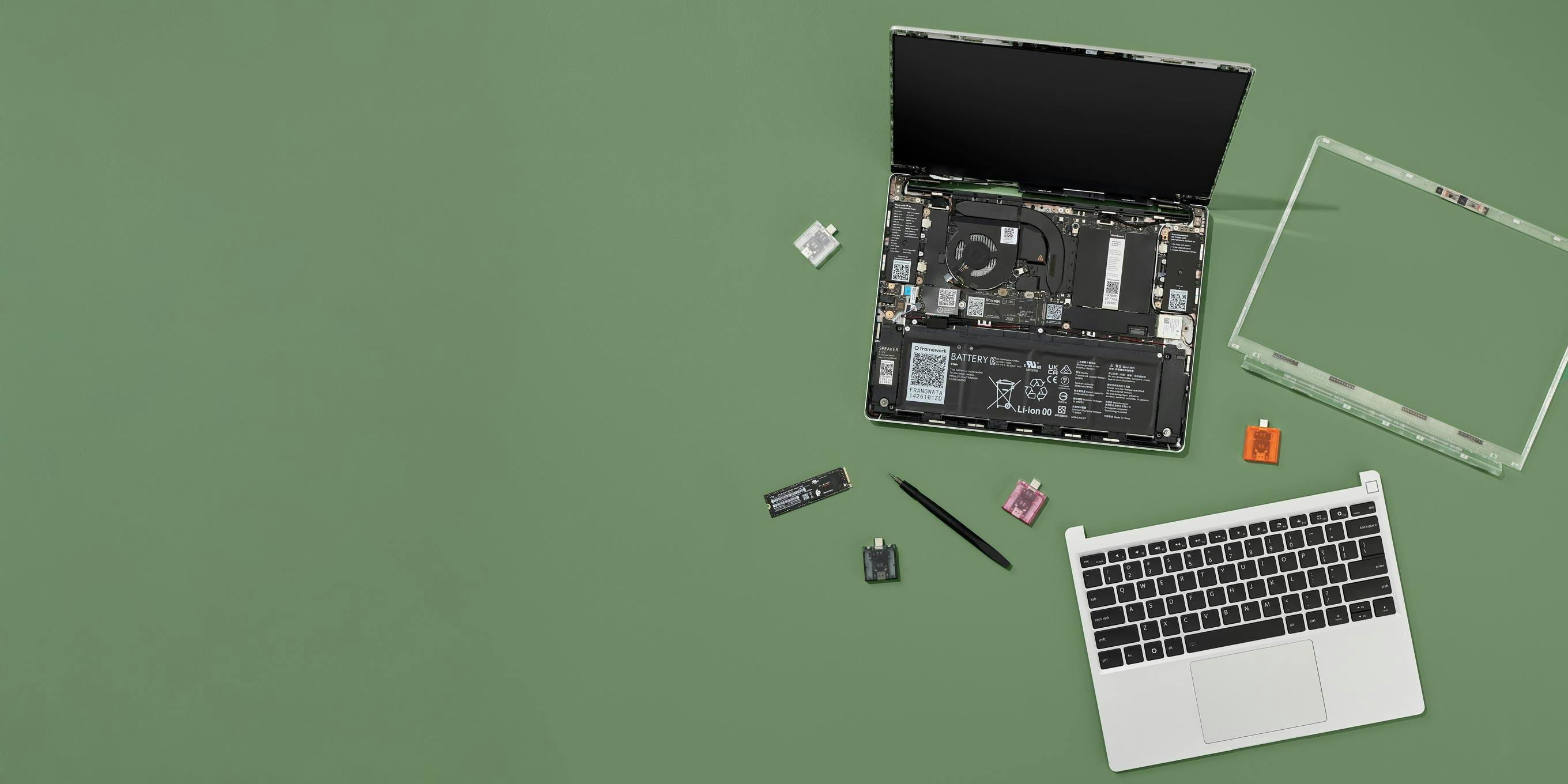 Framework Laptop 13 with bezel and top cover removed, exposing internals with Expansion Cards, screws and screwdriver beside it.