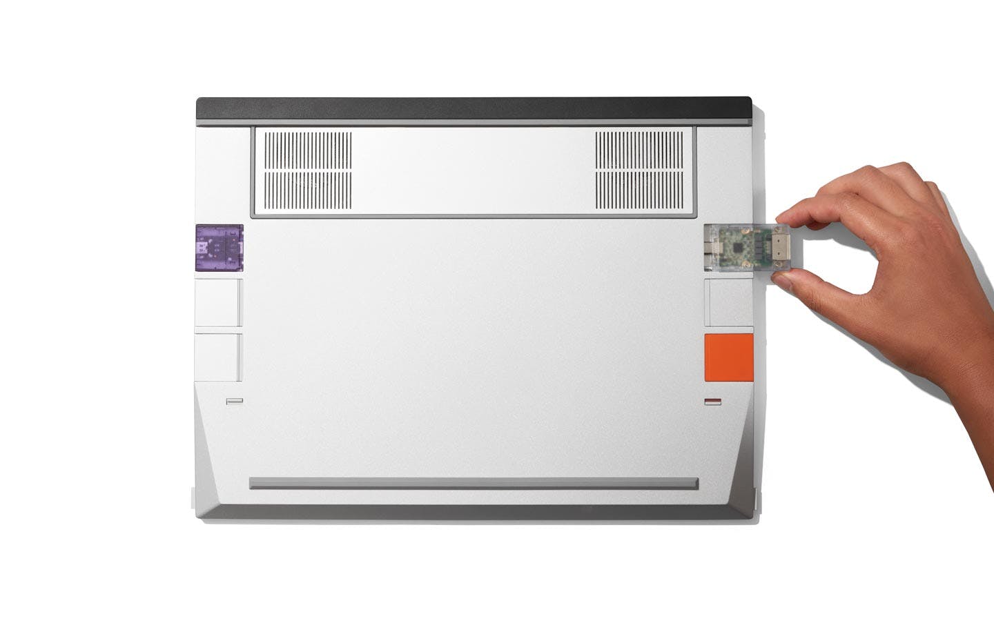 An upside-down Framework Laptop 16, focused on six Expansion Card slots, with a hand installing a translucent-white USB-C card.