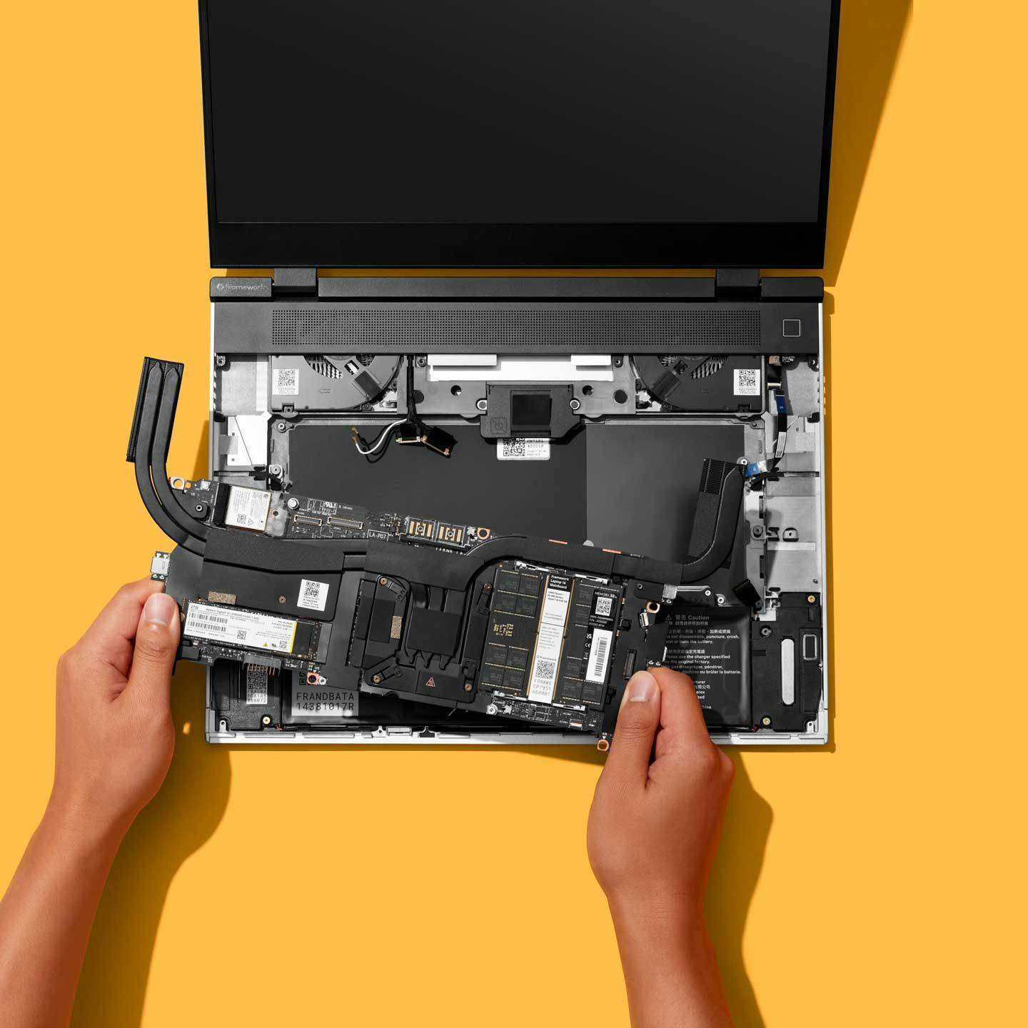 Top-down studio shot of a Framework Laptop 16 with a person installing the mainboard.