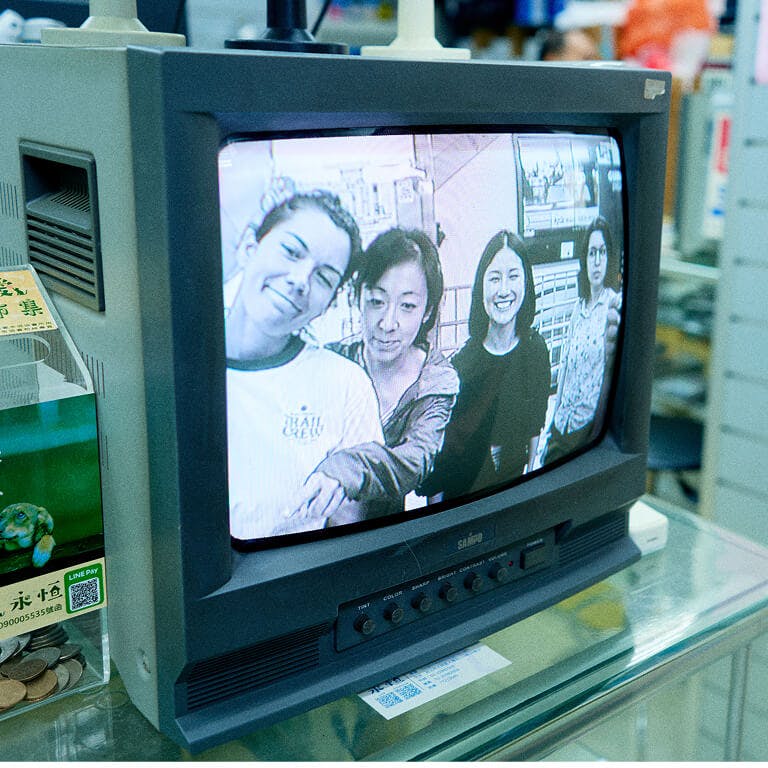 A vintage CRT television monitor sitting on a glass shelf, displaying a black-and-white photograph of four smiling Framework employees on its screen.