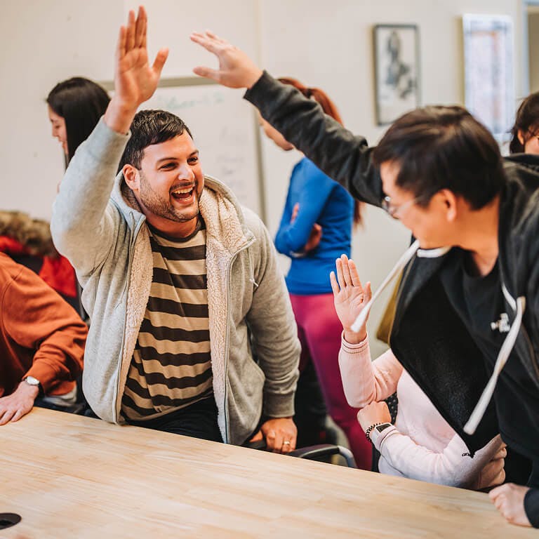 Two smiling Framework employees high-fiving each other enthusiastically in a collaborative office setting.