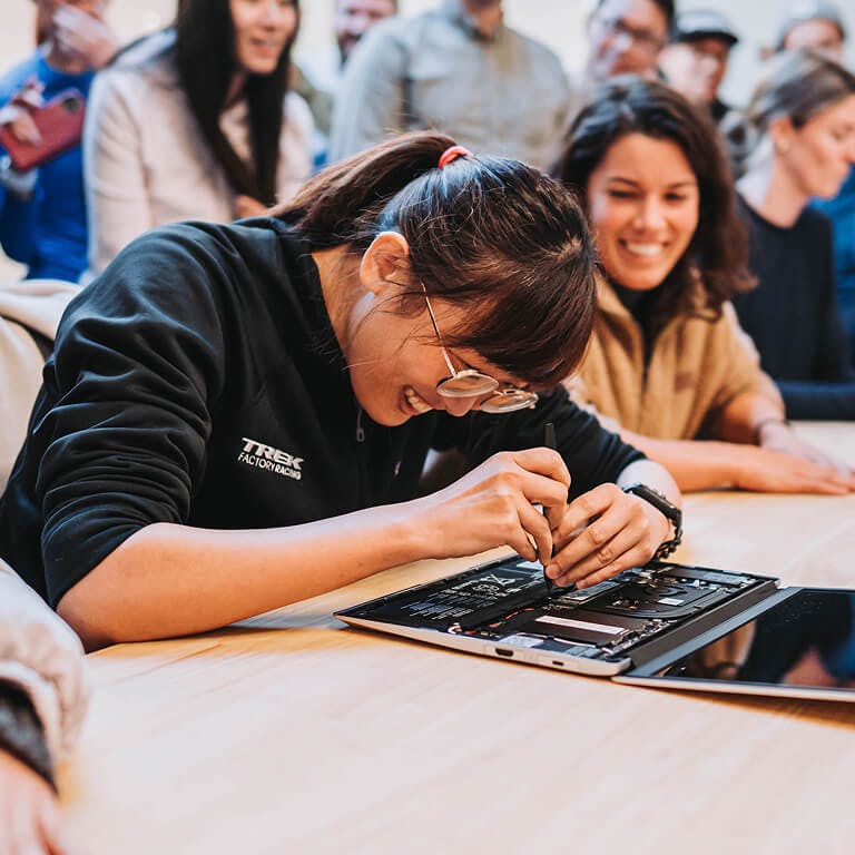 A smiling employee using a tool to work on the internal components of an open Framework Laptop while colleagues watch from the background.