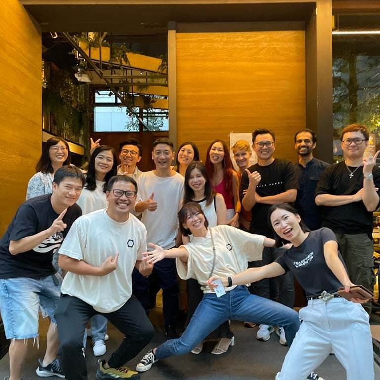 A cheerful group of about fifteen Framework employees posing together indoors, with one team member striking a playful action pose in the foreground.