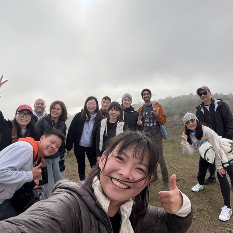 A cheerful group of Framework employees taking a selfie together on a foggy hilltop during an outdoor team hike.