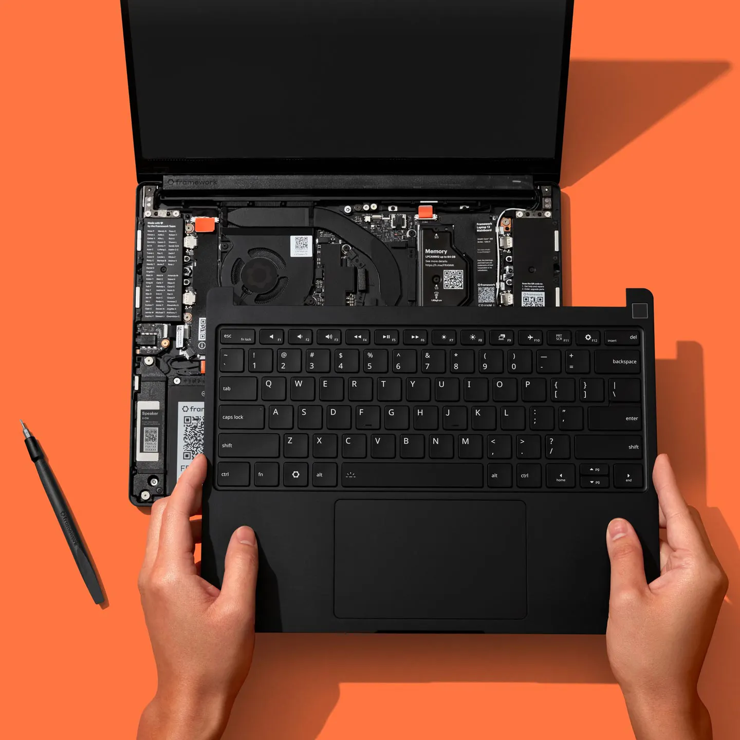 A top-down installation studio shot of a Framework Laptop 13 Pro against a Framework orange backdrop.