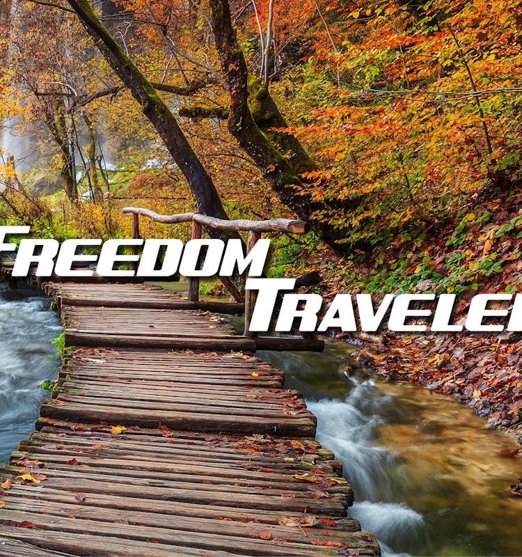 Freedom Traveler with bridge over river leading to a waterfall in the woods