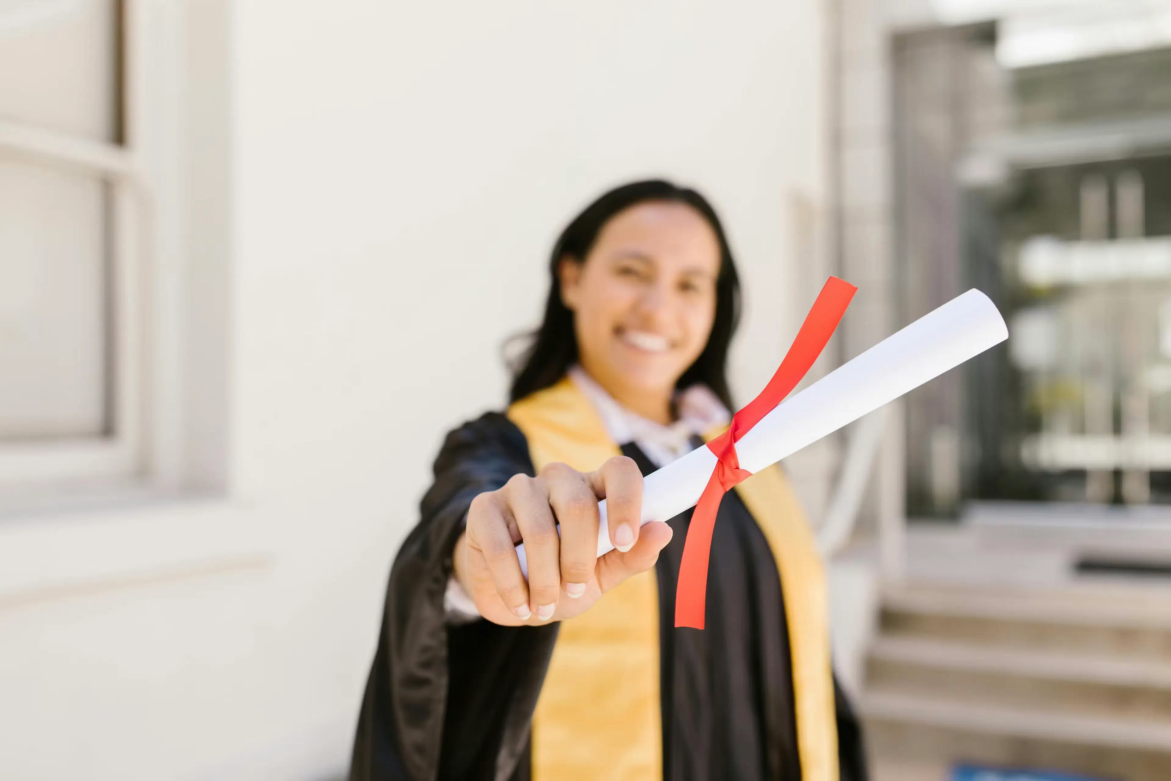 Ragazza mora tiene in mano pergamena di laurea avvolta da un nastrino rosso