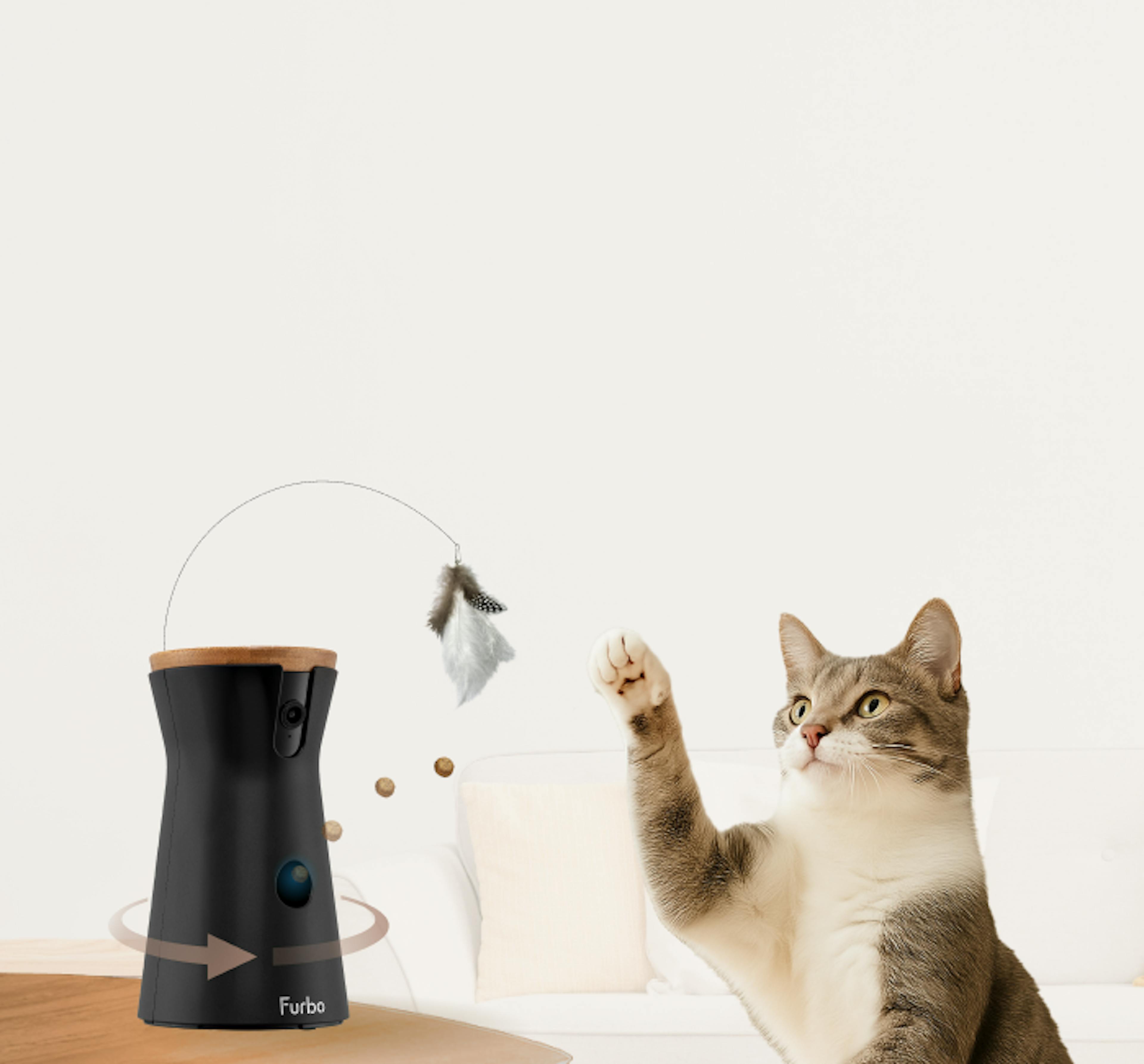 Furbo 360° Cat Camera on a wooden table with a curious cat peeking up from the edge, looking at the device. 
